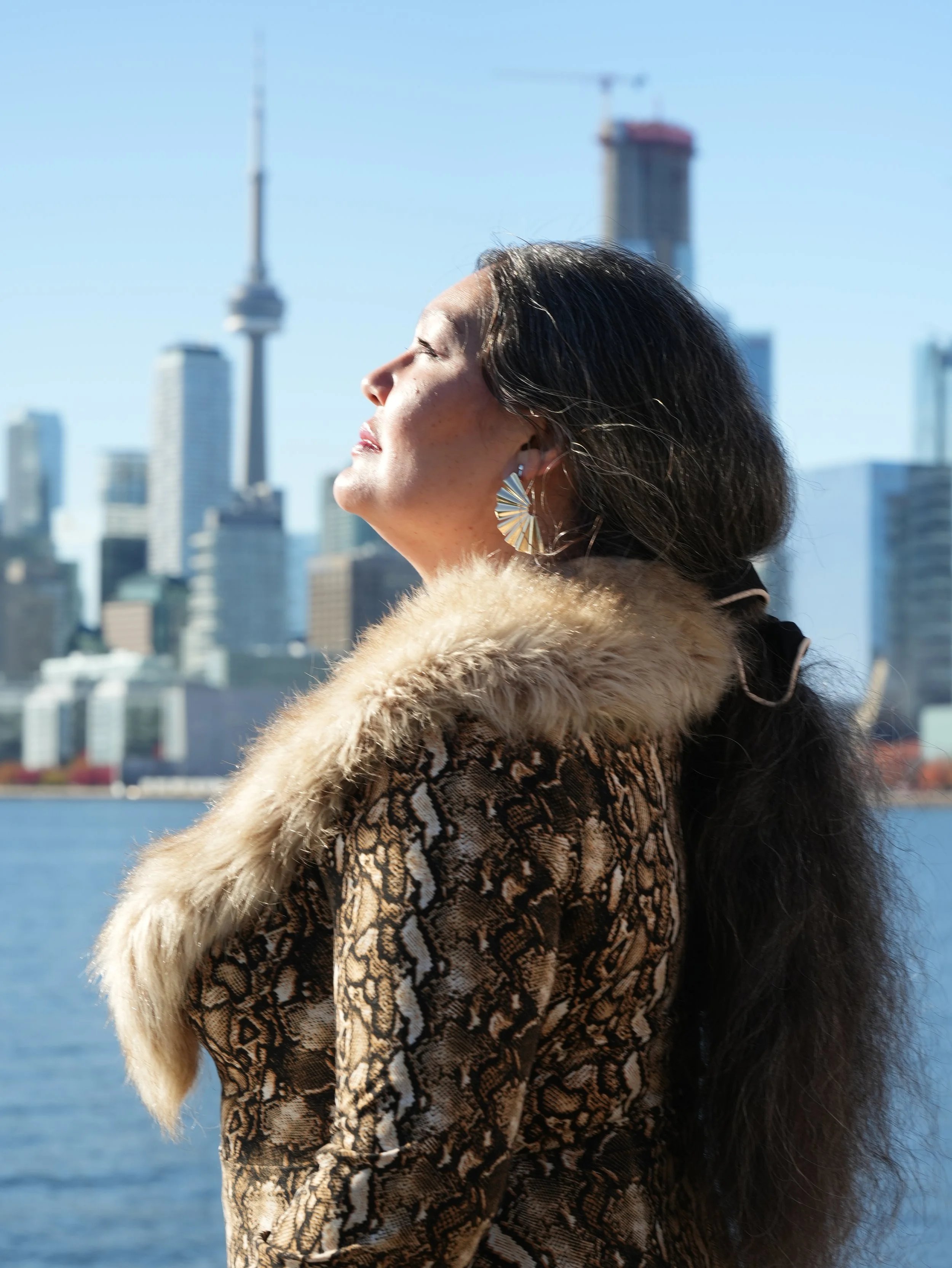 Woman with glasses holding them with both hands, looking up, wearing earrings and a teal top with embroidery, with text "who's your favorite?" overlayed.