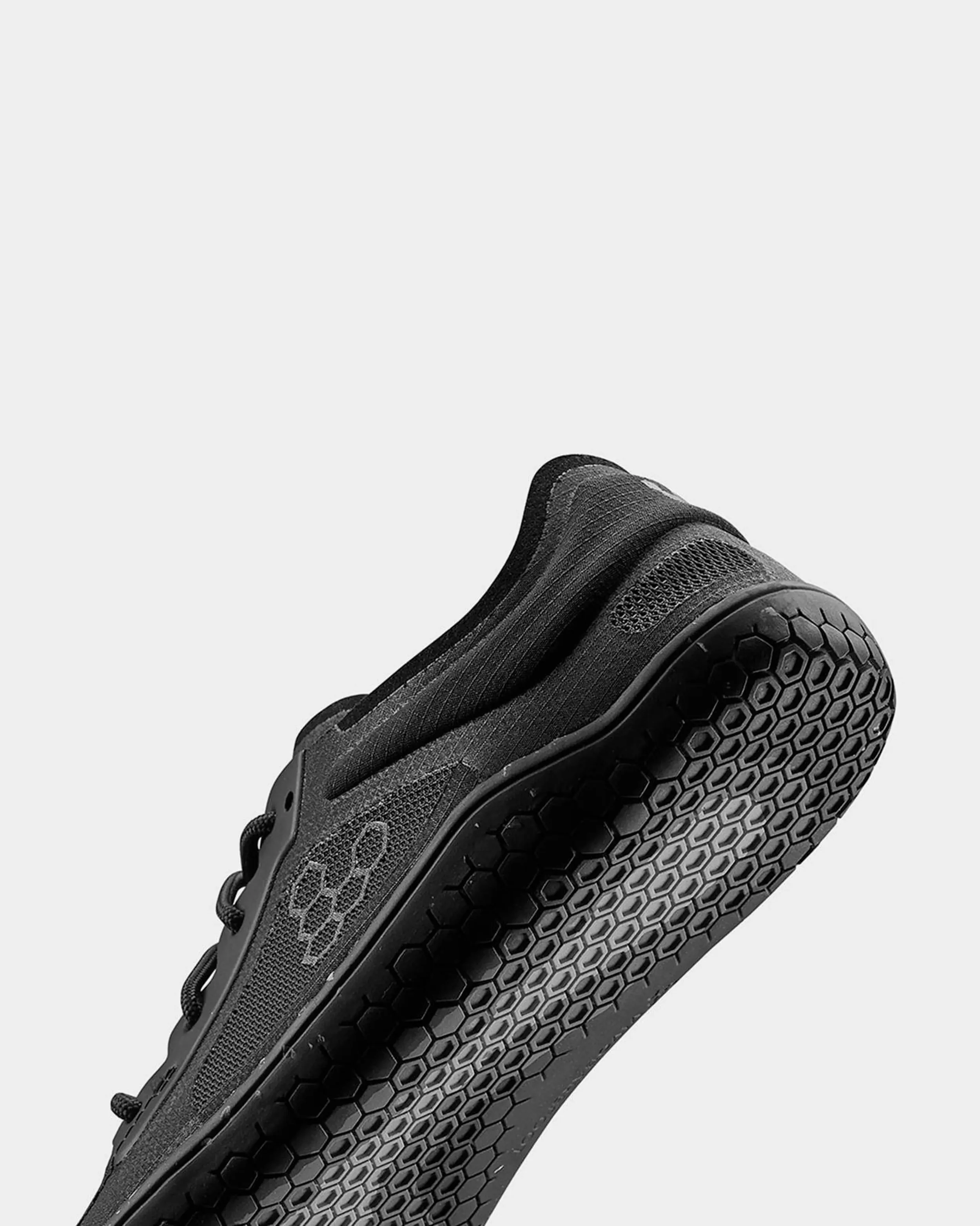 Close-up of a black athletic shoe with a honeycomb-patterned sole against a plain background.