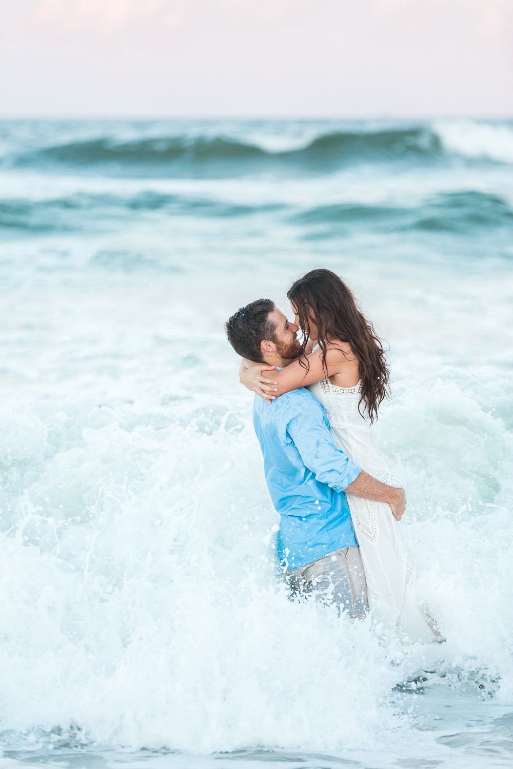 engaged couple running in the ocean and kissing