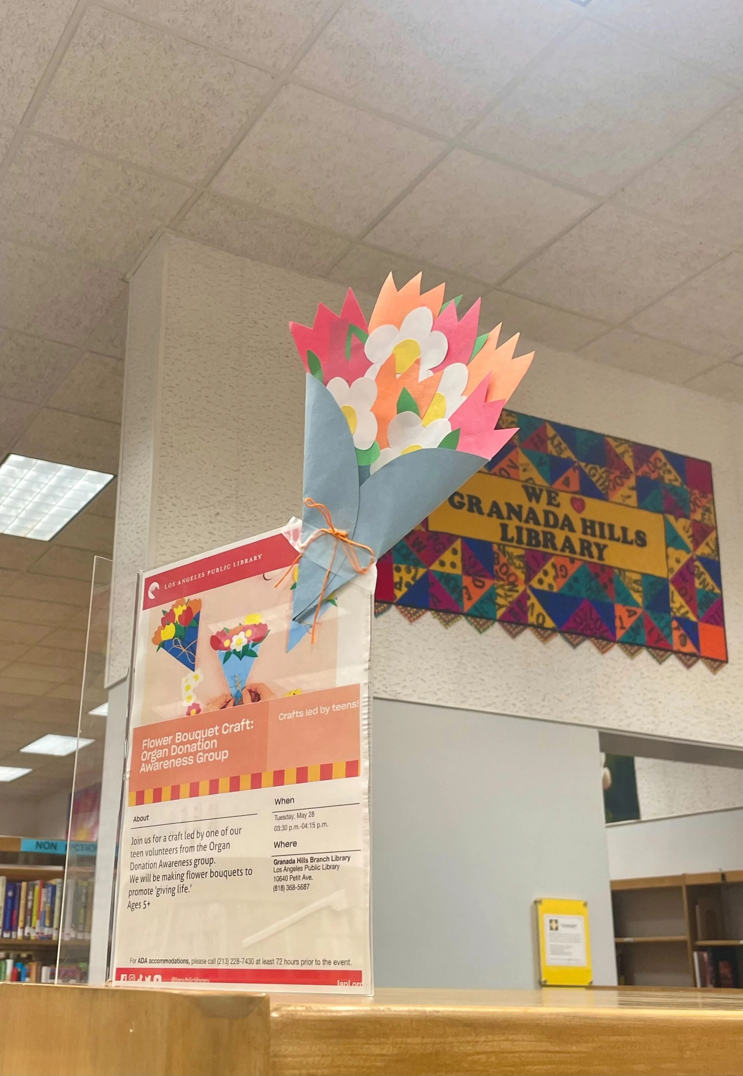 Colorful paper flower bouquet displayed above an event poster at Granada Hills Library.
