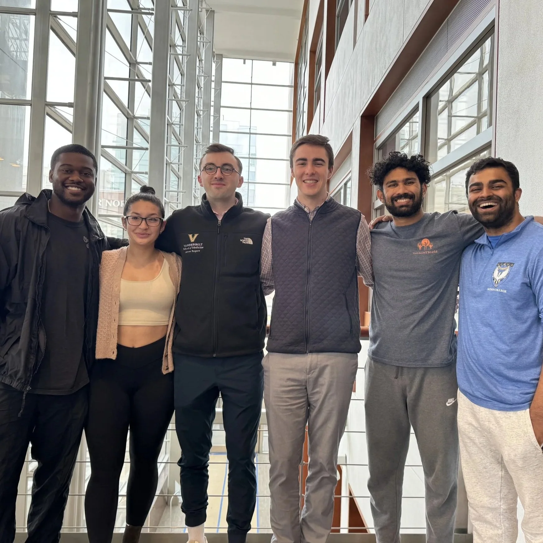 Group of six diverse young adults standing together indoors, smiling for the camera.