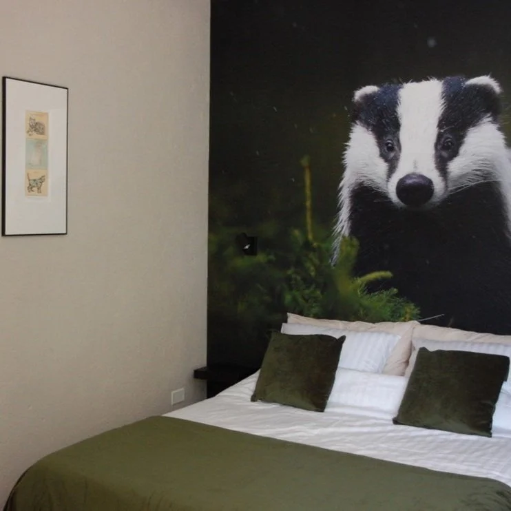Slaapkamer met bed, groene kussens, een muurdecoratie van een das en een ingelijste afbeelding aan de muur.
