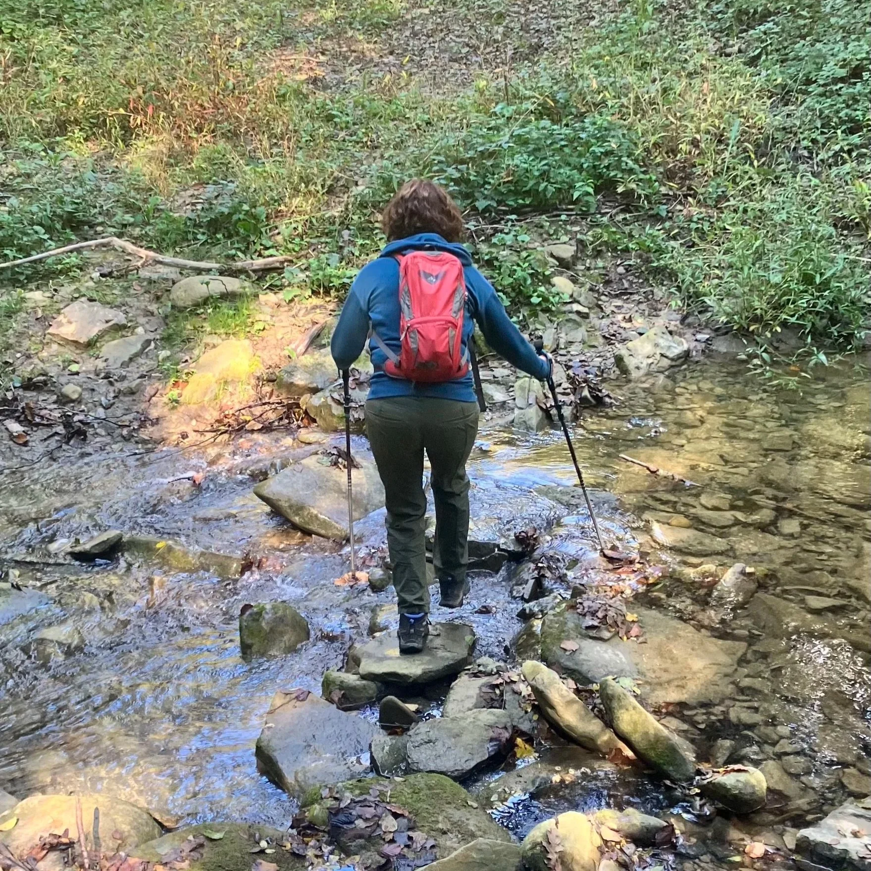 Vrouw met wandelstokken steekt stroompje over