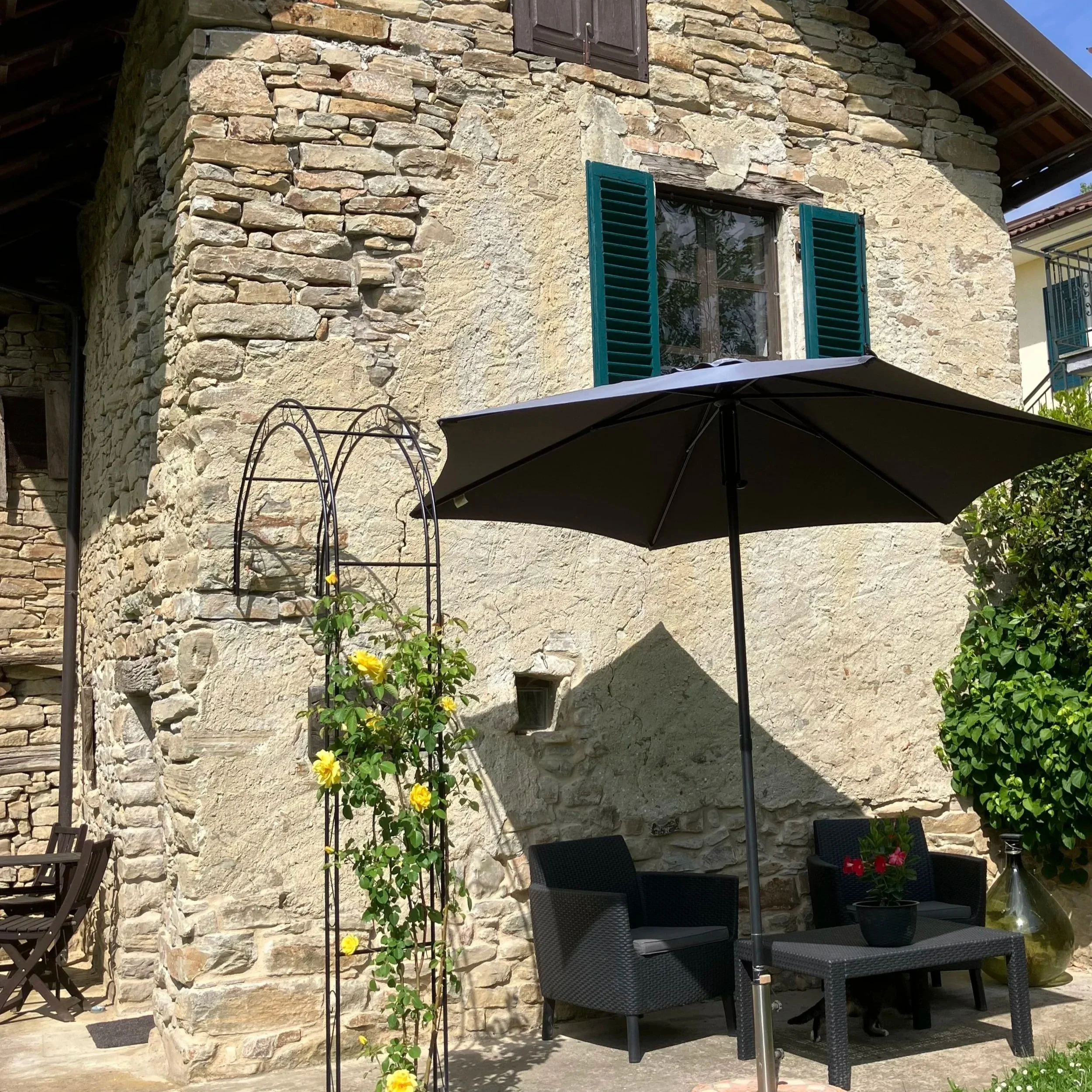 Oude stenen huis met houten meubels en parasol in de tuin.