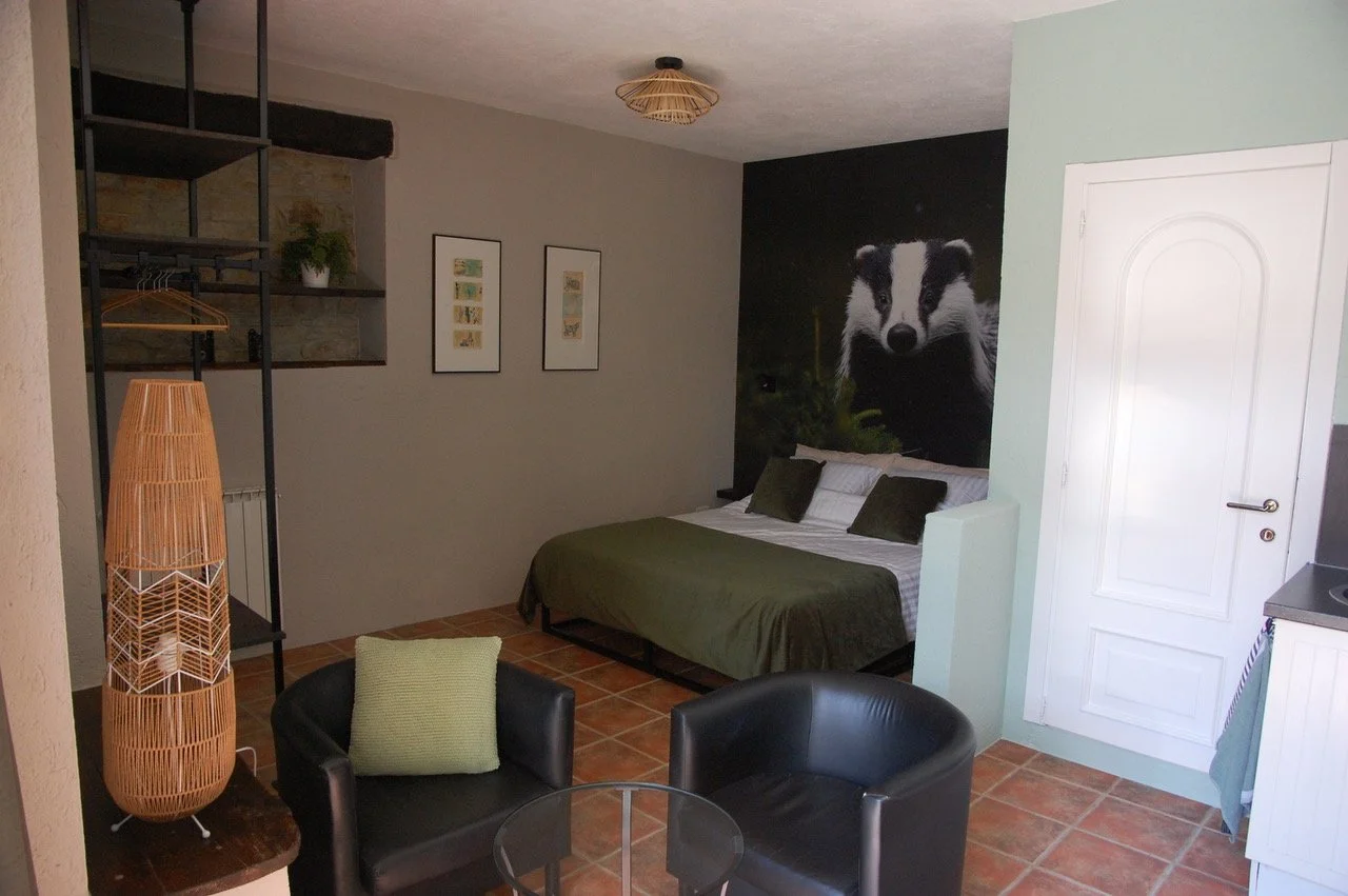 Interieur van een slaapkamer met een bed, groene kussens, een muurposter van een das, zwarte fauteuils en een glazen tafel, met decoratieve elementen en een hanglamp.