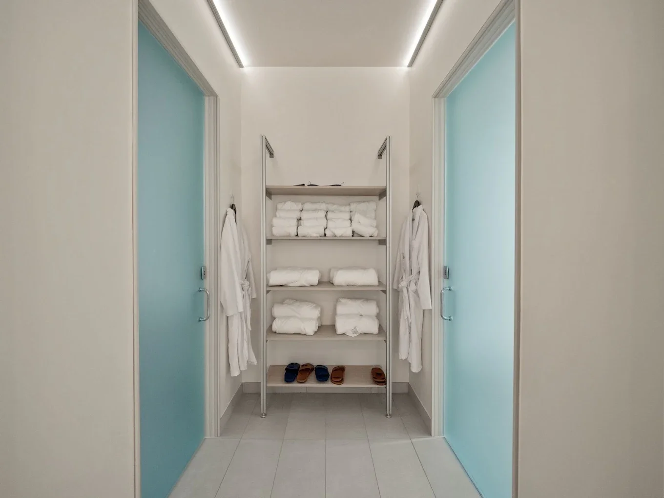 Empty white tiled shower with black fixtures, a small bench, and three black pump bottles on the wall.