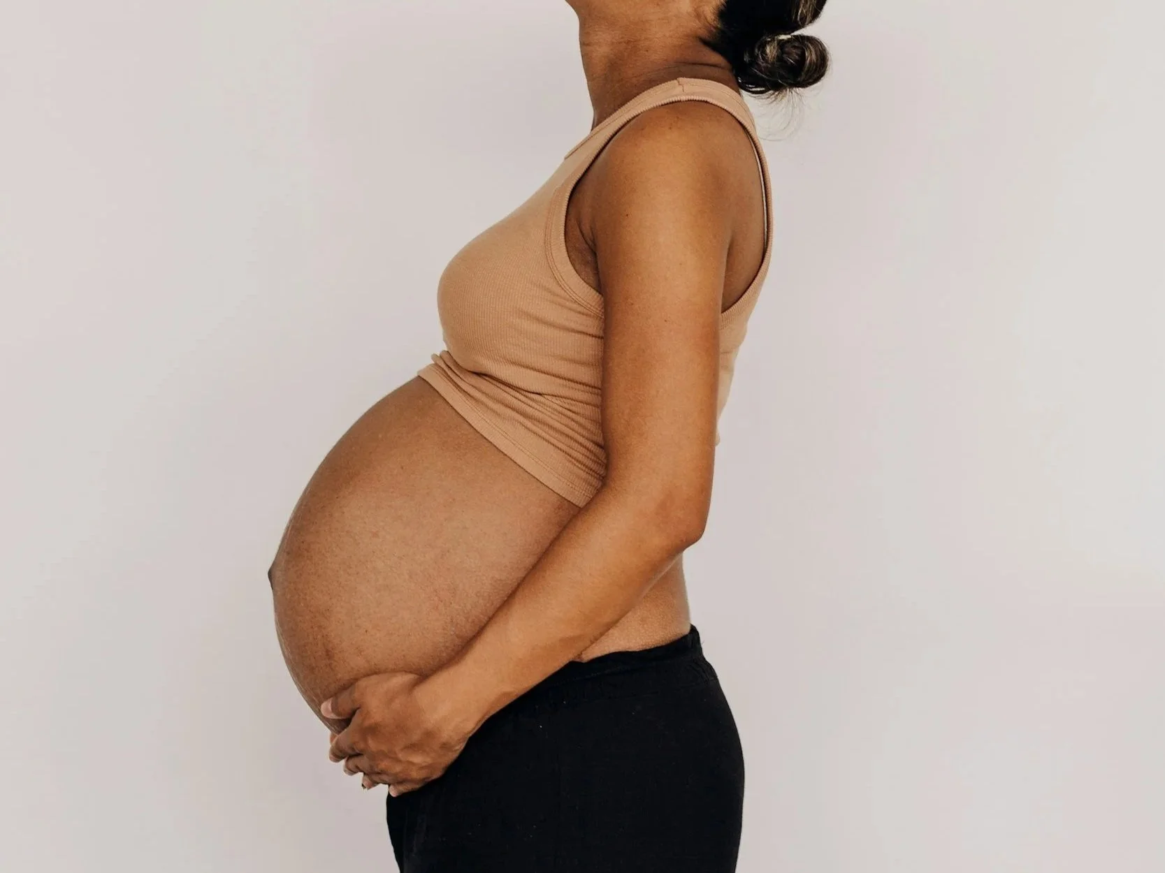 Close-up of a pregnant woman lying on a bed, wearing a black tank top and black underwear, with a visible baby bump.