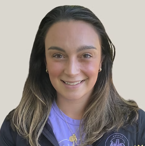 Smiling woman with shoulder-length hair wearing a purple shirt and a dark jacket, against a plain background.