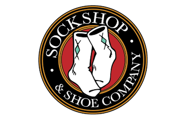 A young woman with shoulder-length black hair, smiling and showing her teeth, wearing a dark blue top, surrounded by green plants.