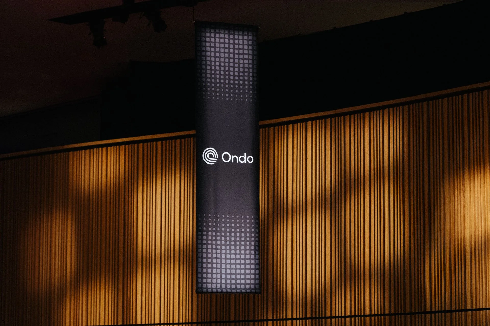 An illuminated vertical sign with the logo and name 'Ondo' displayed on a dark background, mounted on a wooden wall with vertical slats.