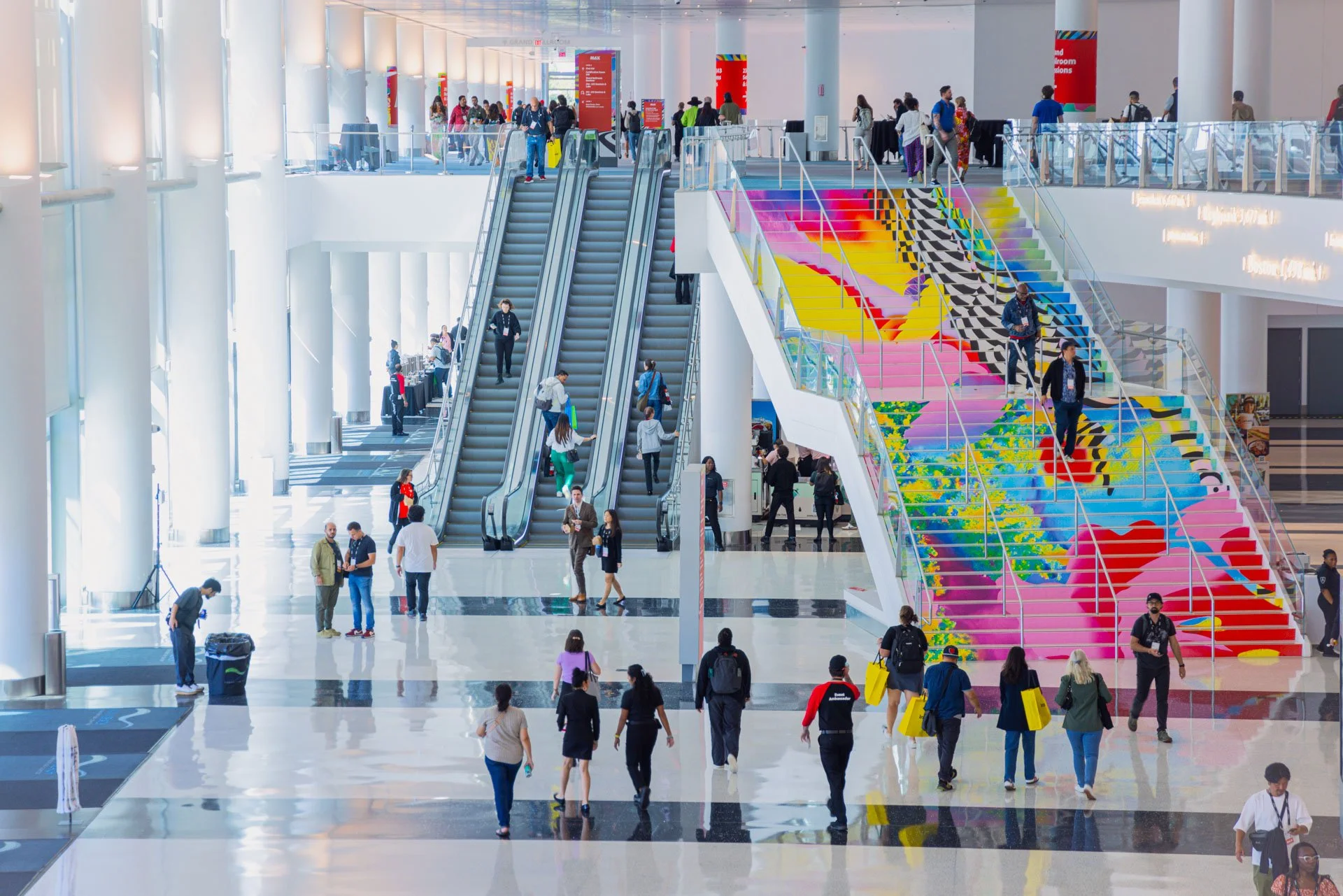 People walking through a spacious, modern airport terminal with colorful staircases and escalators. Photography of Adobe Max conference in Miami for Play.Studio.  High end branding and corporate event photography.