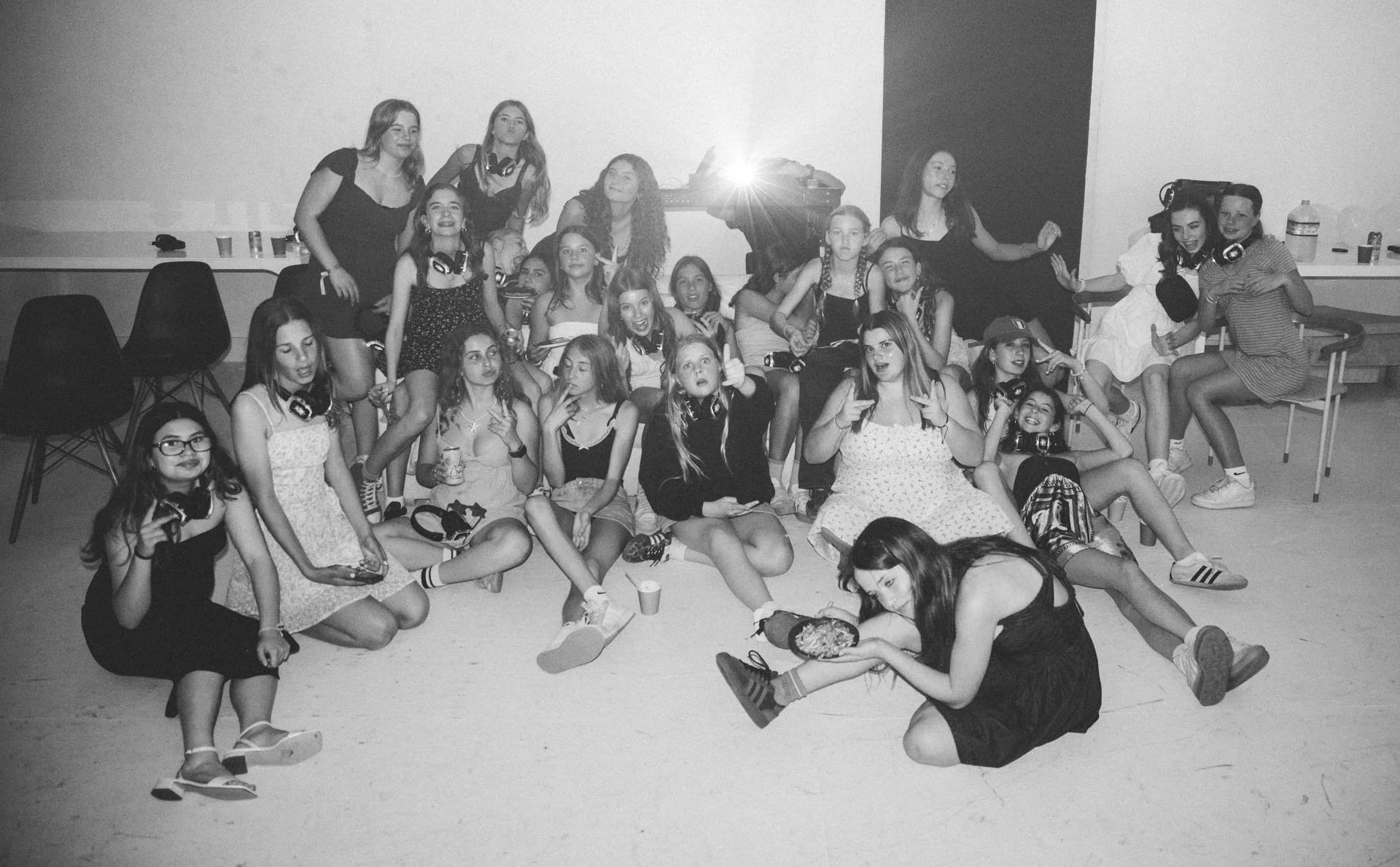 A group of young girls at a birthday party, some sitting and some standing, with food and drinks around them in a hall or community room.