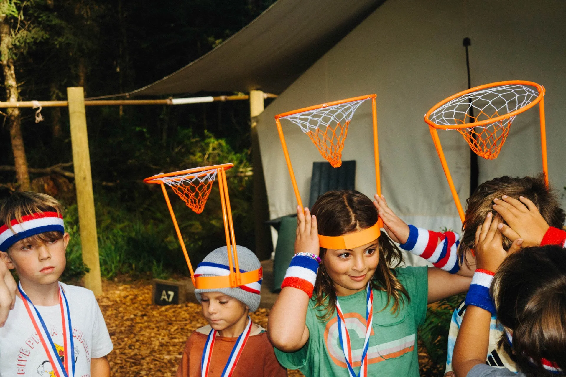 Children wearing orange basketball hoop headbands at a camp or outdoor event.
