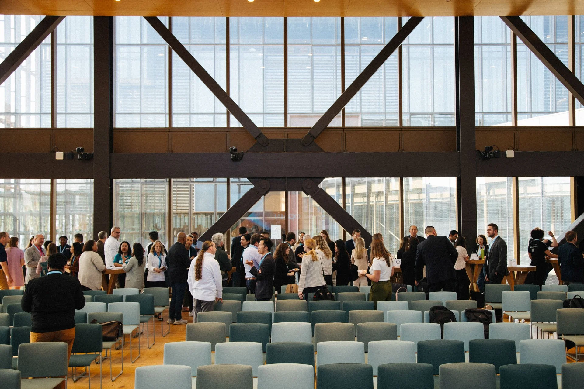 Conference or business event with many people mingling and chatting indoors in a large, modern space with glass walls and high ceilings.