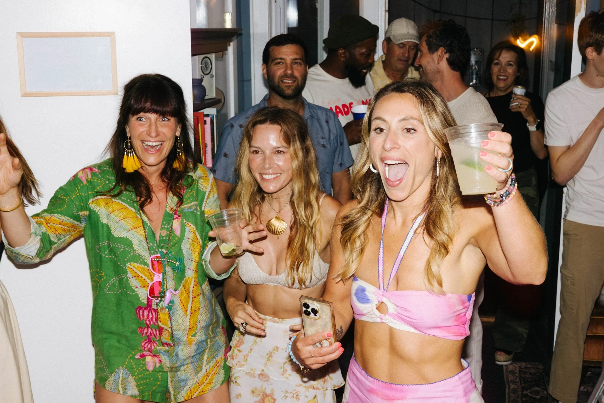 Group of people enjoying a party indoors, some holding drinks, smiling and engaging with each other.