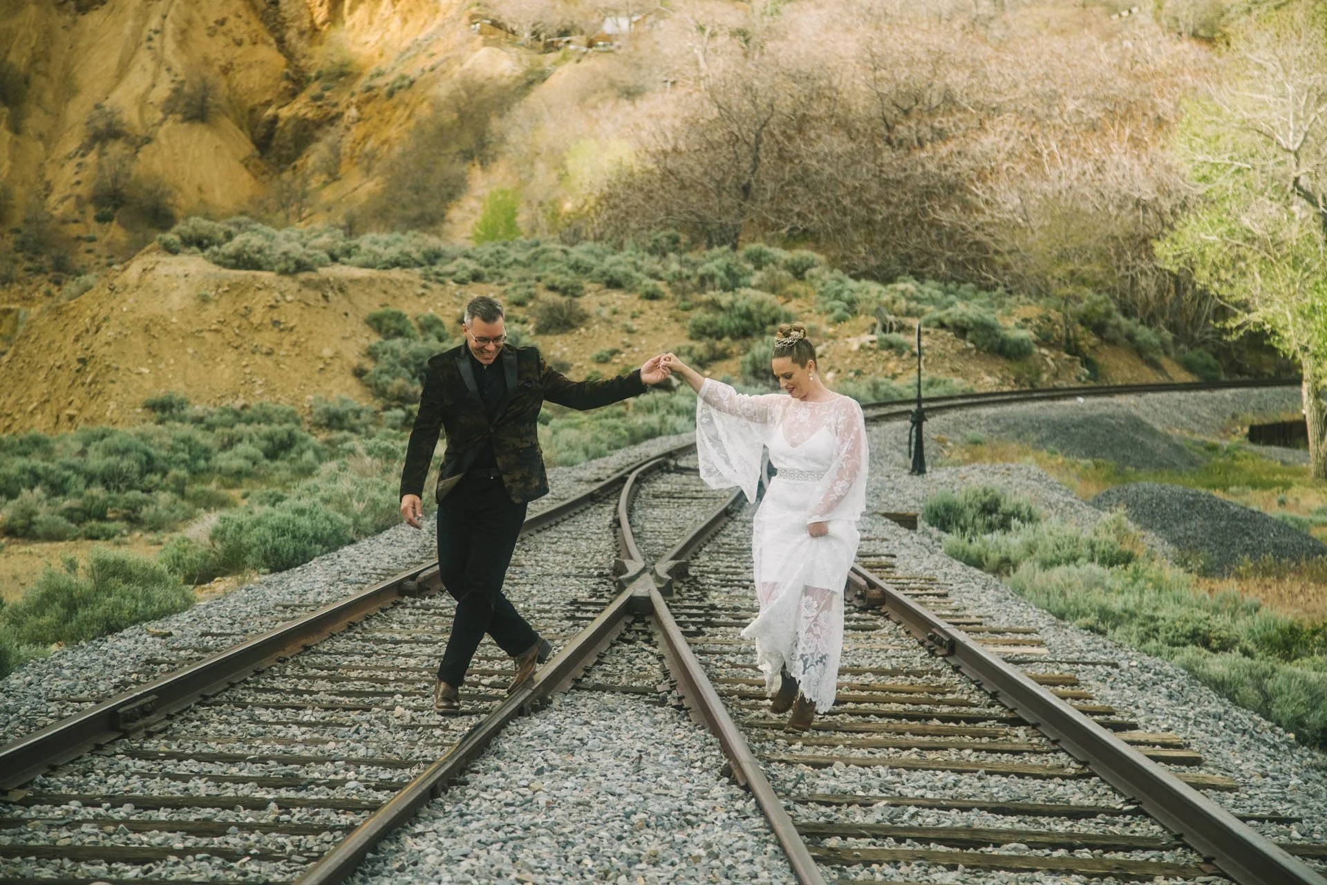 A couple in wedding attire dancing on train tracks with a scenic outdoor background.