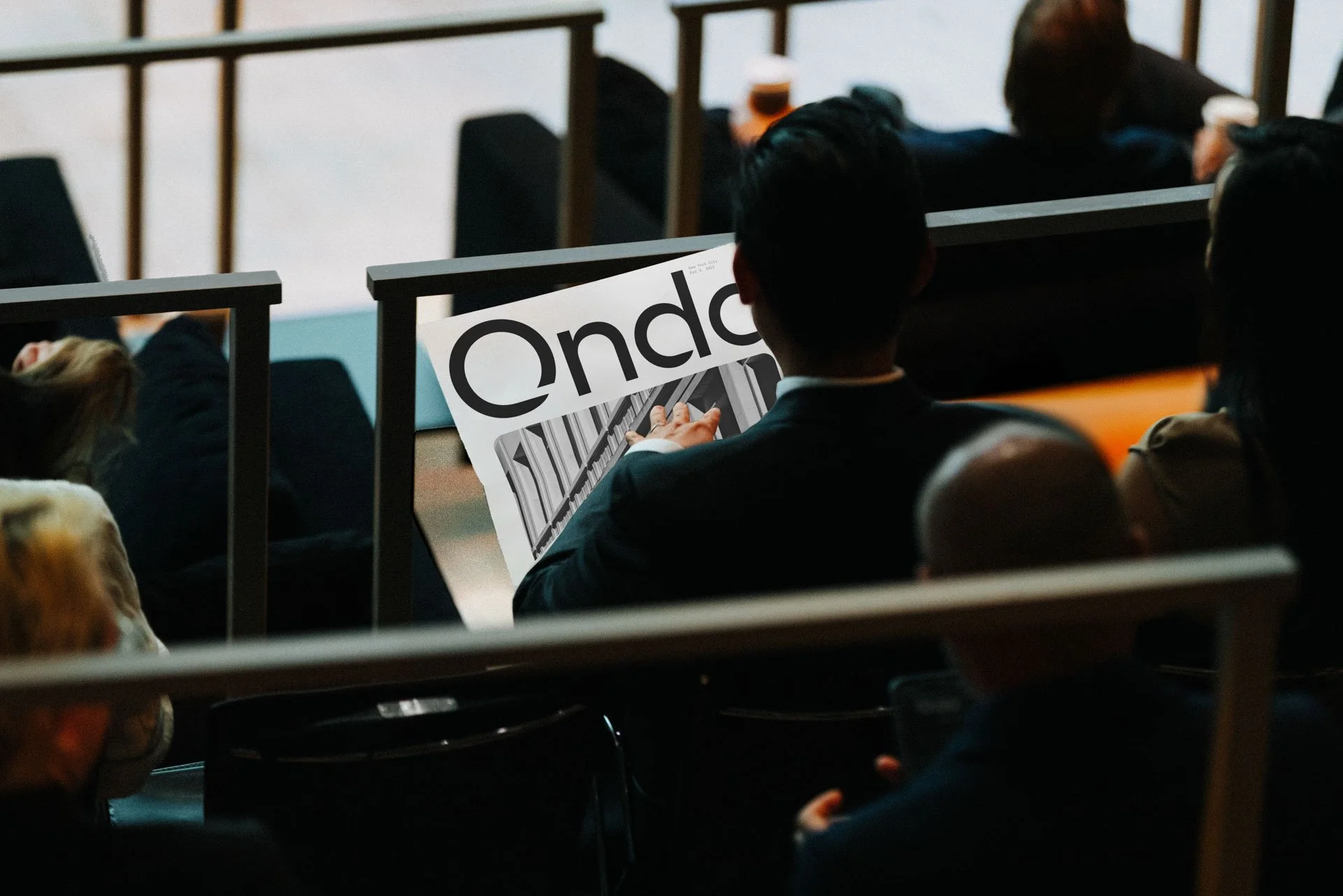 A person in a suit is sitting in a lecture hall, reading a newspaper with the word 'Endo' on the front page.