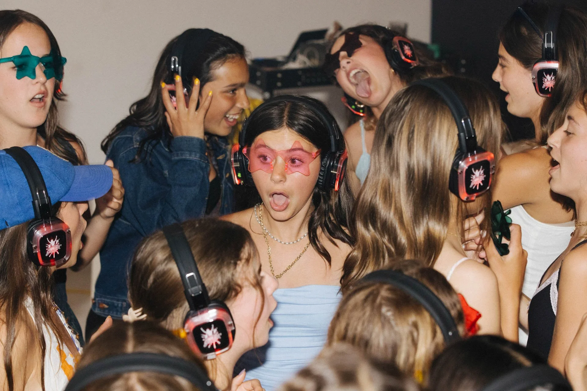 Group of young girls at a party wearing headphones, some singing and dancing
