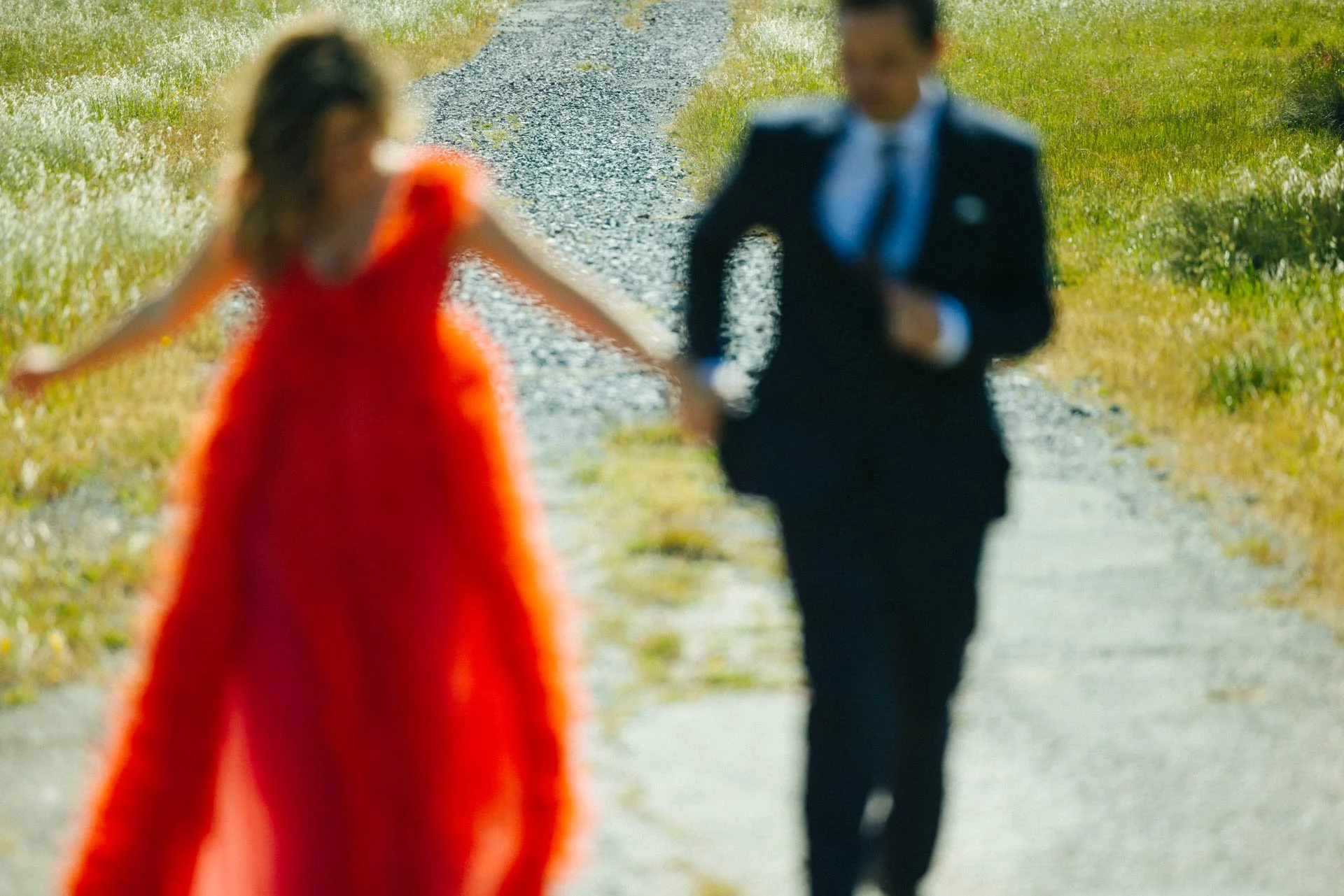 A woman in a red dress and a man in a black suit walking on a country road, holding hands.