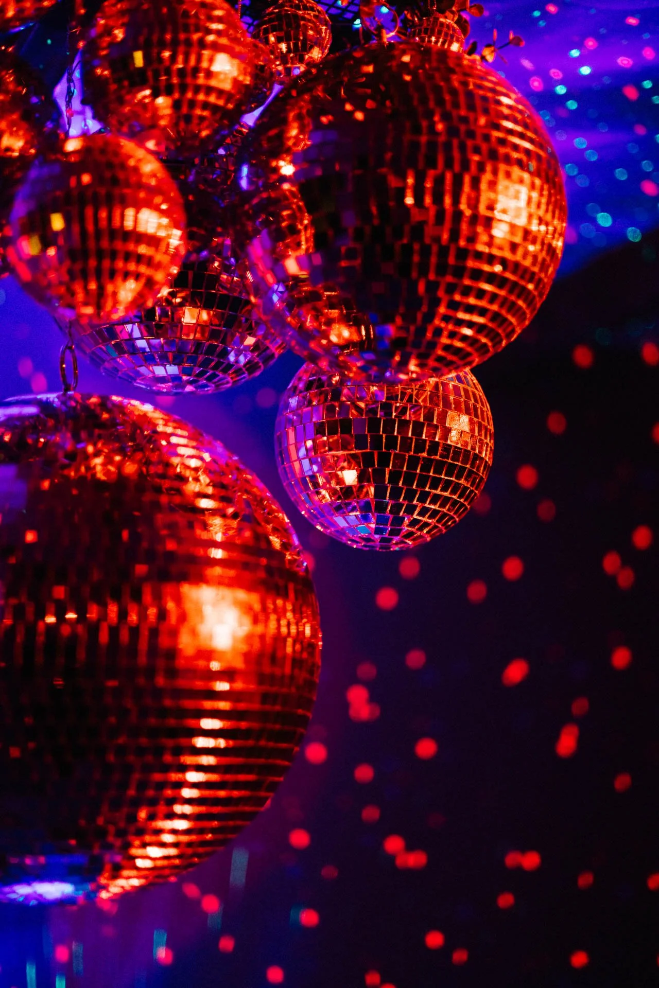 Multiple red disco balls hanging against a dark background with colorful reflections.
