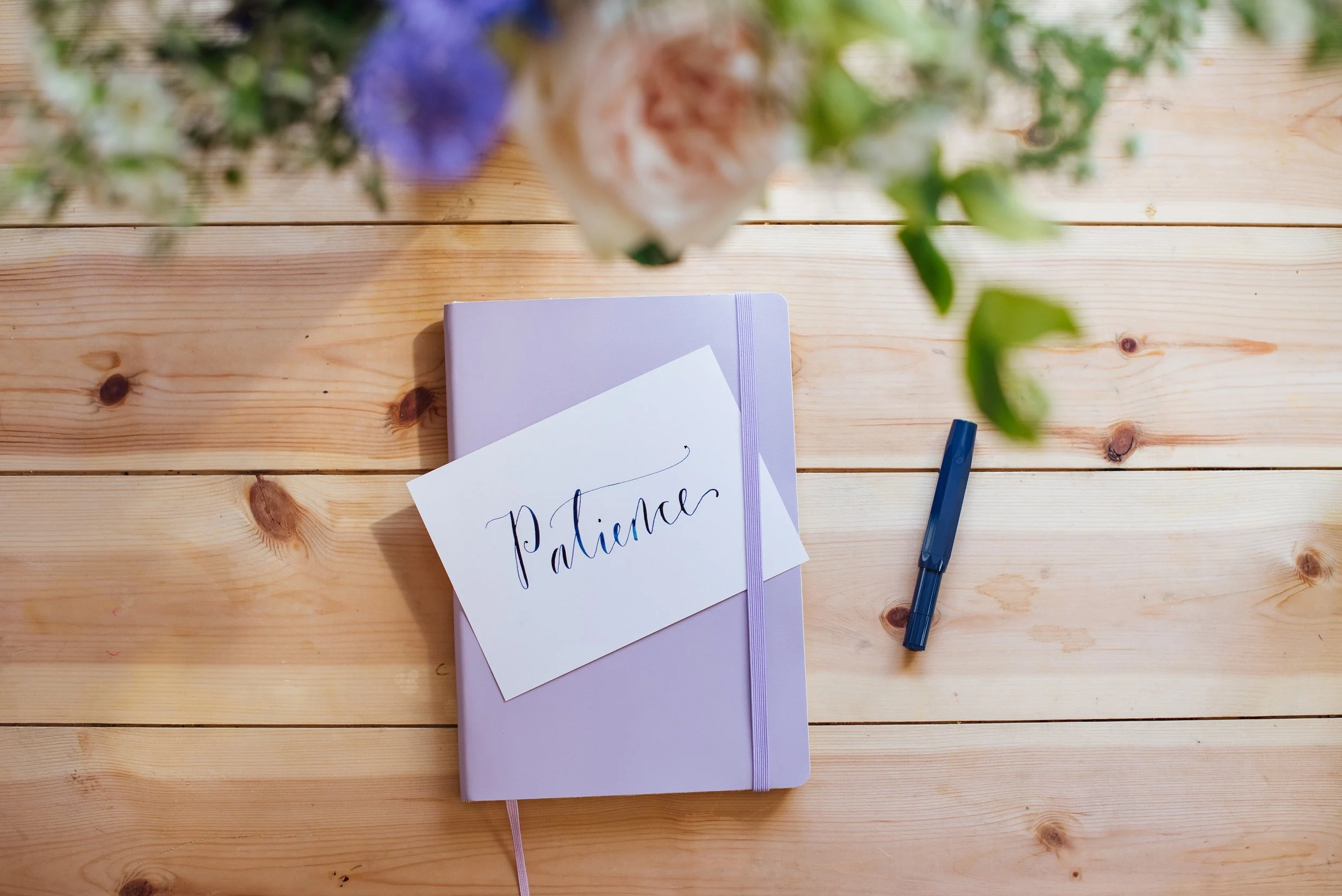A serene postcard visual containing handwritten text that reads patience, used as a grounding reminder for mental wellbeing.