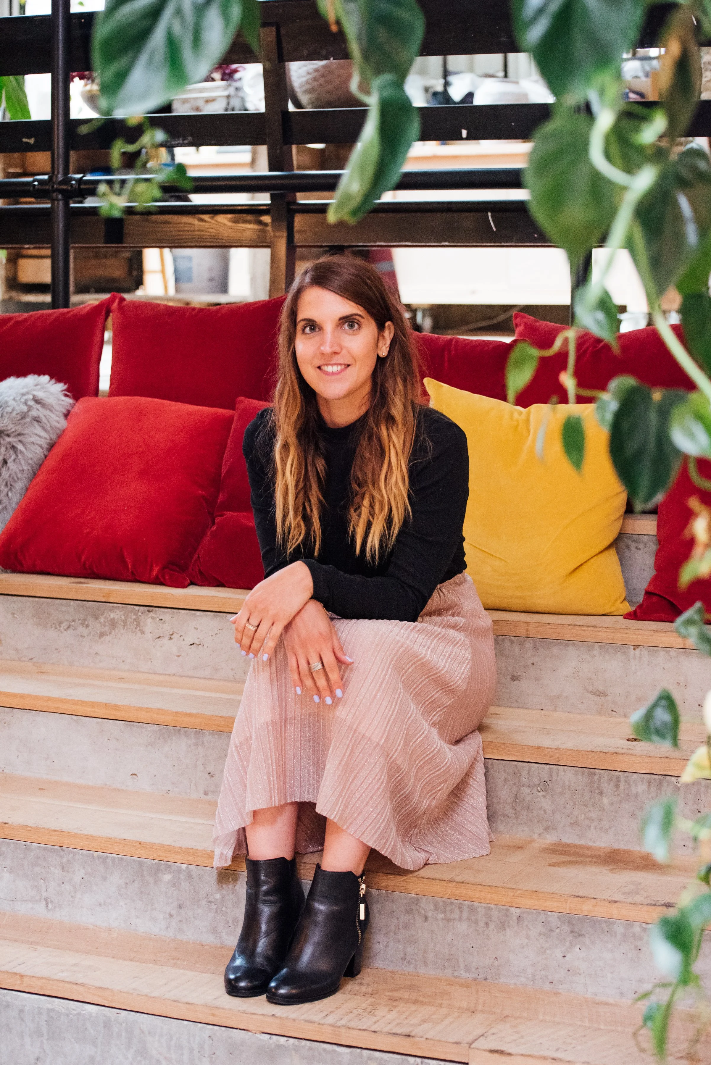 A warm portrait of London hypnotherapist Daniela Bragato sitting on indoor steps, smiling at the camera.