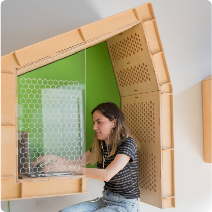 Mujer trabajando en un espacio de trabajo en una cabina de madera con fondo verde, usando una computadora portátil.