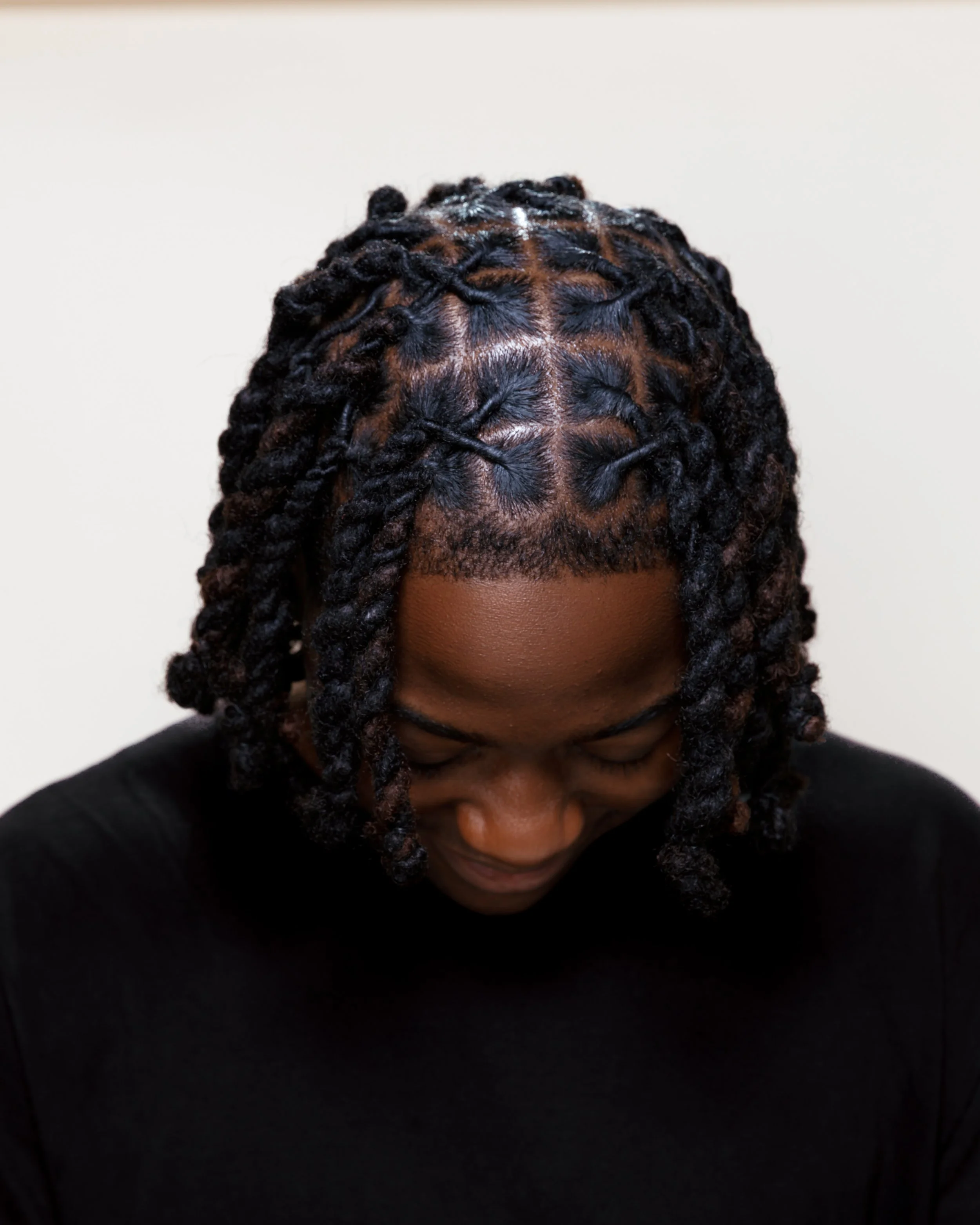 Top view of a person with styled dreadlocks wearing a black shirt, looking down.