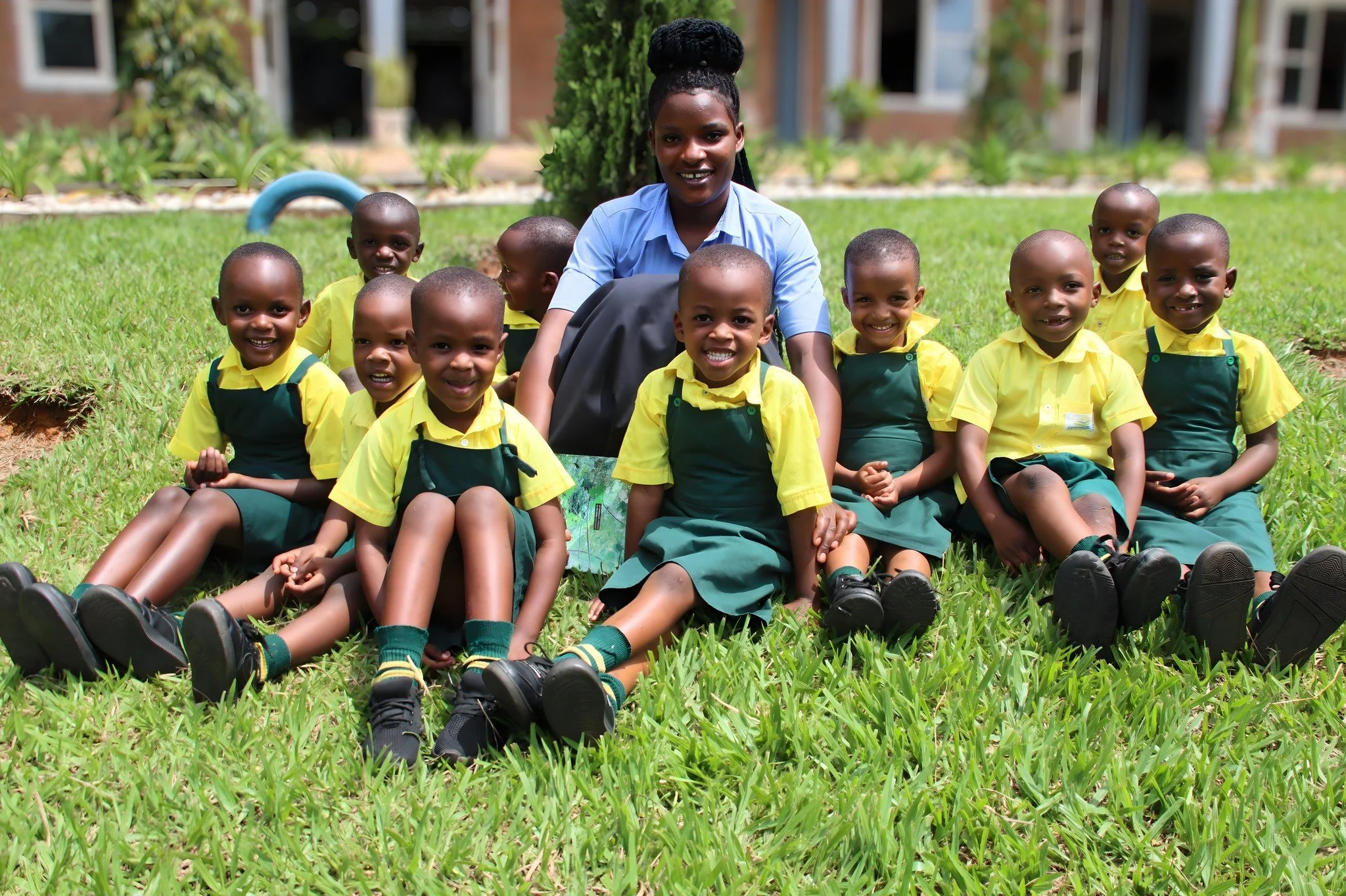 Early Childhood Development teacher Solange Nyirahabimana and some of her students soak up the warm sunshine during recess, enjoying a peaceful break on one of our campus&rsquo;s lush green lawns. Moments like these remind us why a safe, nurturing en