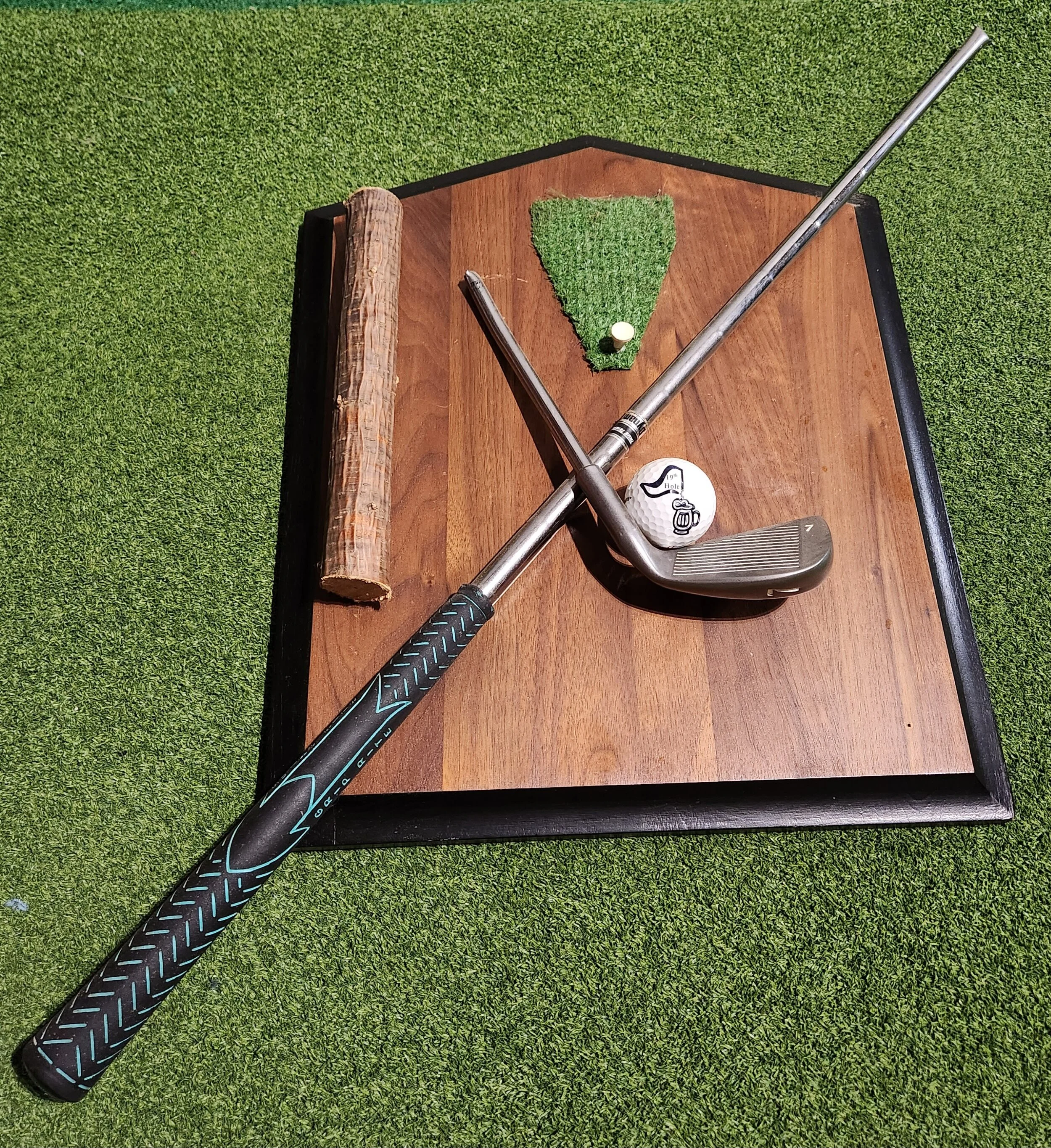 A golf club and a wooden piece on a wooden board with artificial turf and a golf ball with a cartoon design.