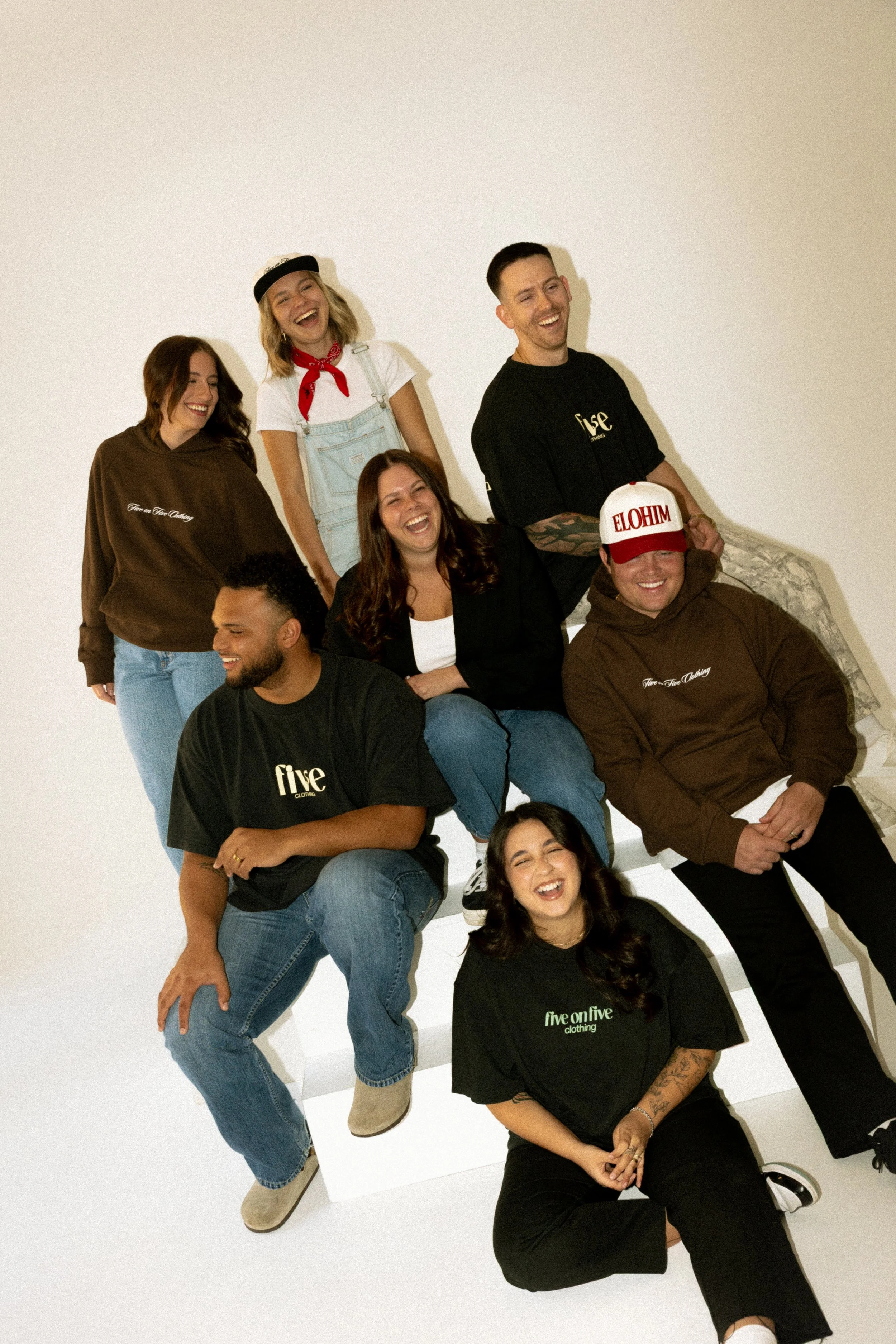 Group of eight young adults smiling and posing together in a studio with a white background.