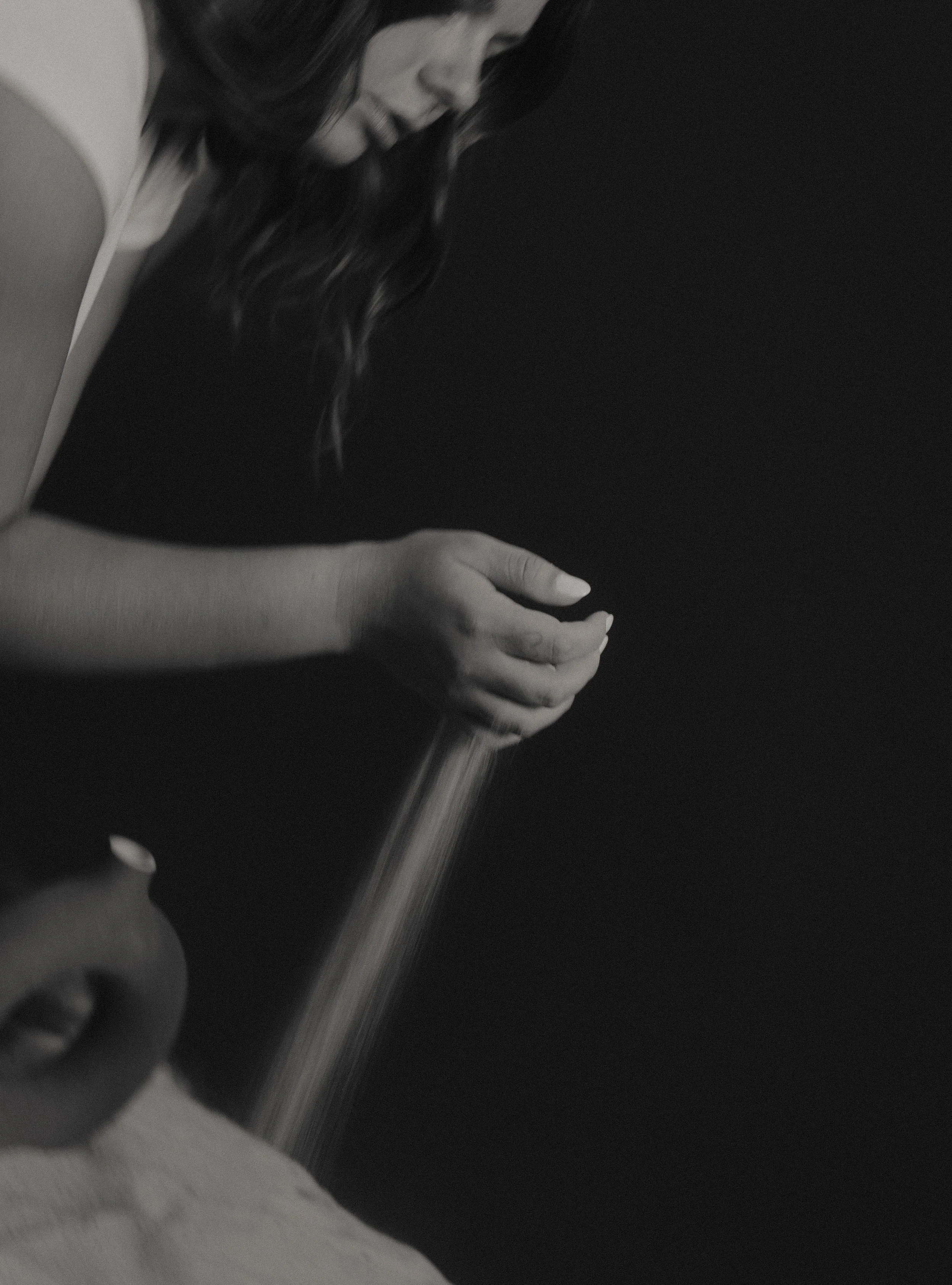 A woman with long, wavy hair pouring sand onto a person's arm in black and white.
