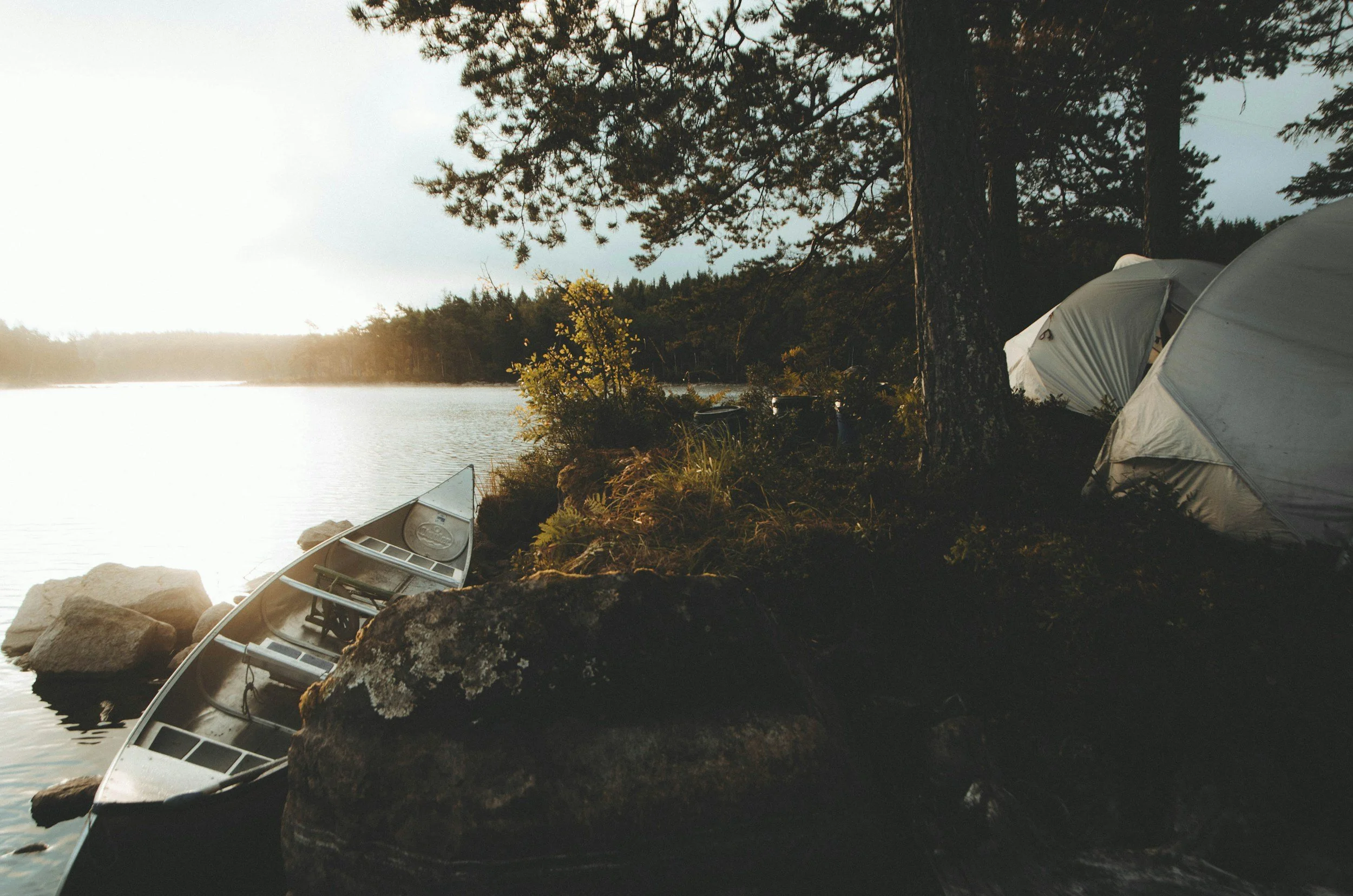 A canoe and tent on the edge of a lake.