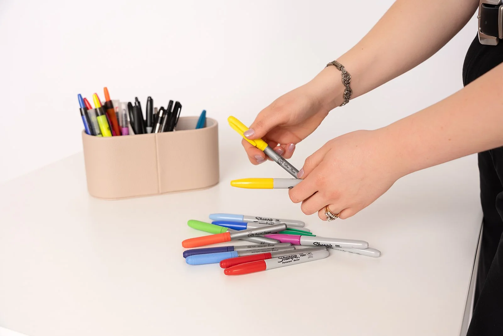 A woman holds different colored markers, sorting them in front of a marker organizer.