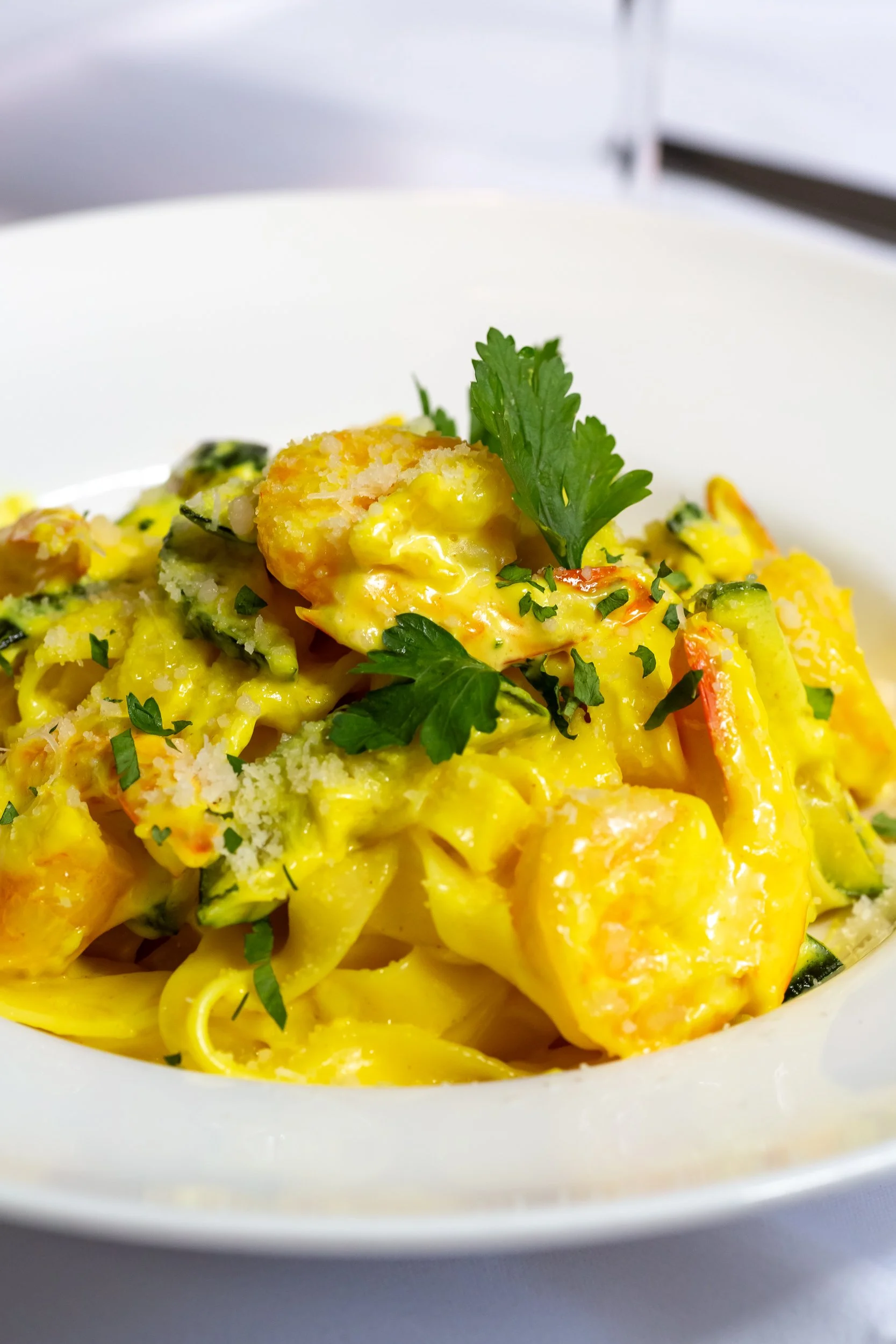 Close-up of tagliatelle with courgette and prawns in a white bowl.
