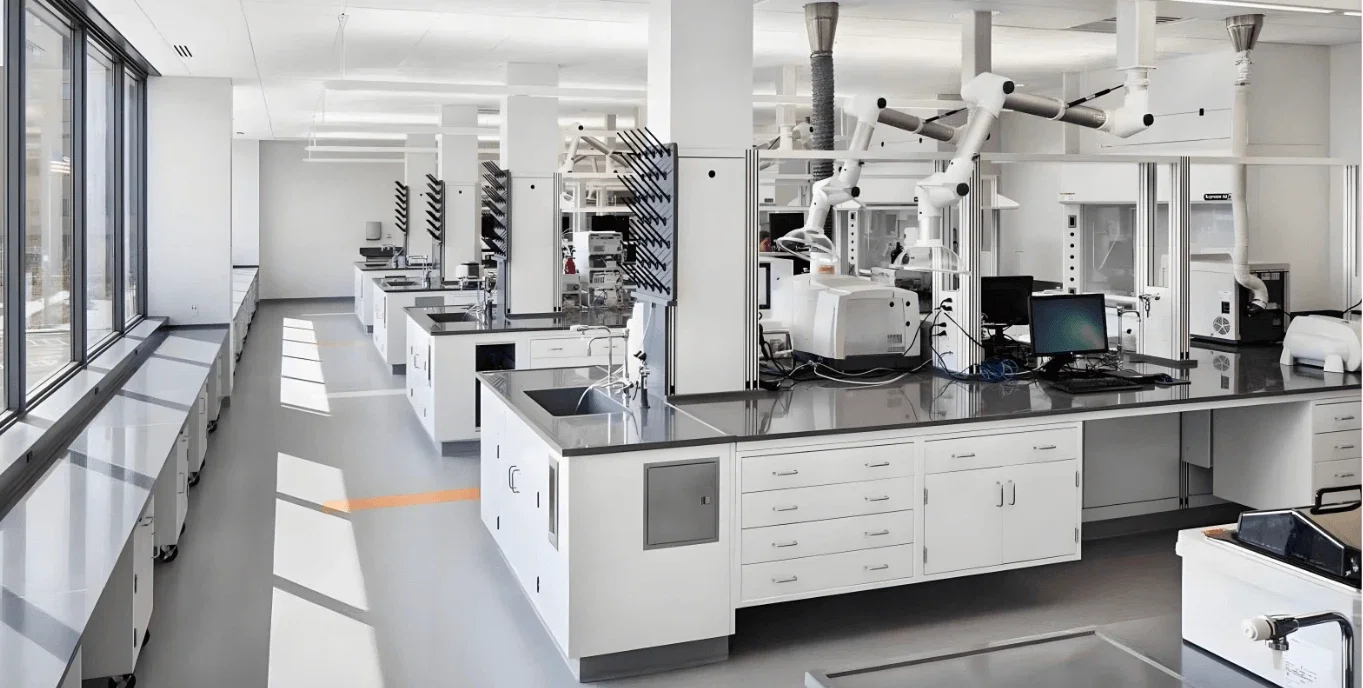 Modern scientific laboratory with white countertops, scientific equipment, and robotic arms, illuminated by natural light through large windows.