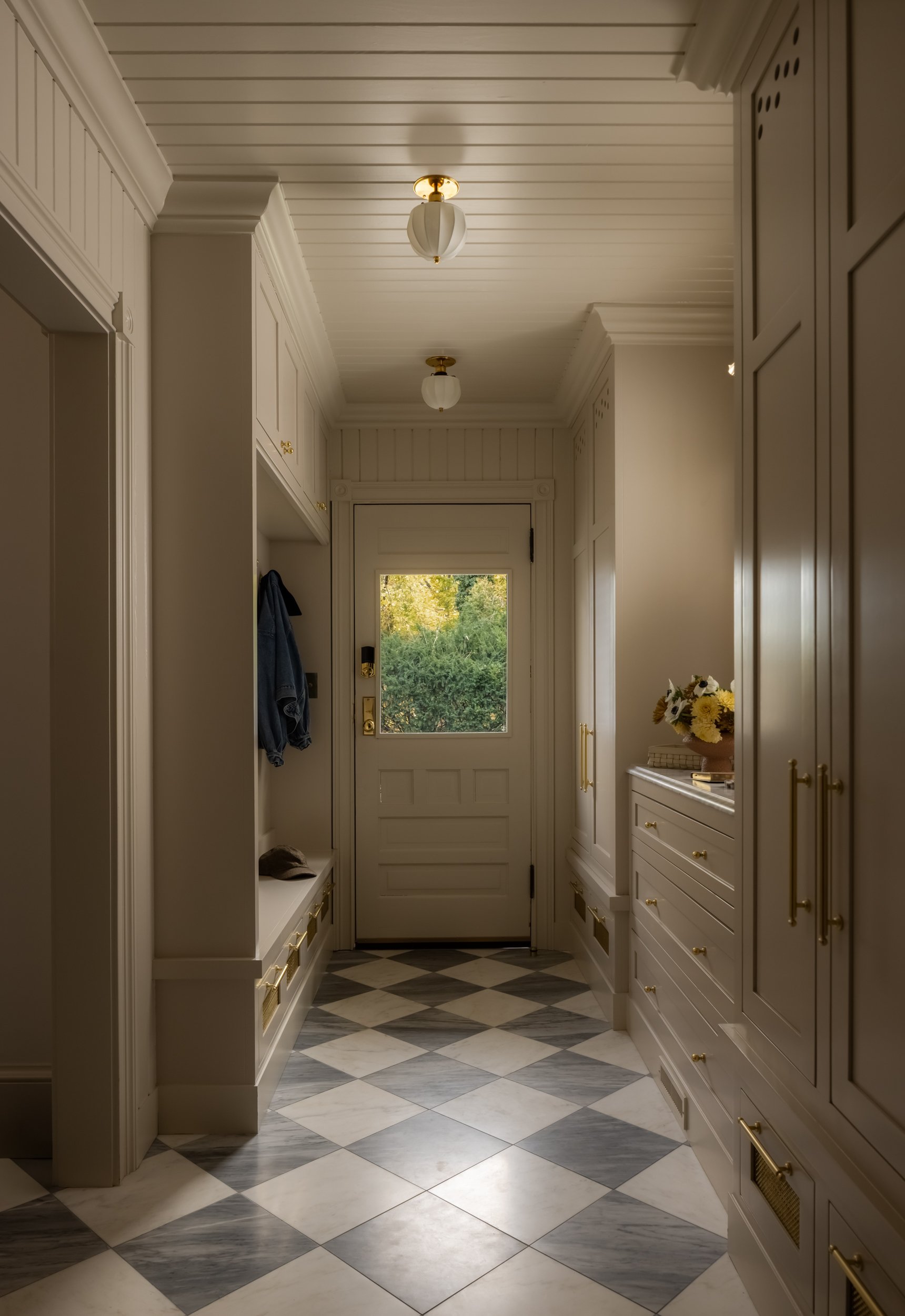 Dramatically lit mudroom featuring classic checkered marble floor tiles and a warm, glowing light. Photographed in Long Island, NY, by Raquel Langworthy and featured on The Wall Street Journal.