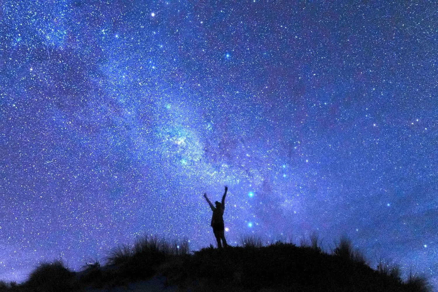 A person raising two hands up to a starry night sky with the most beautiful star formation above