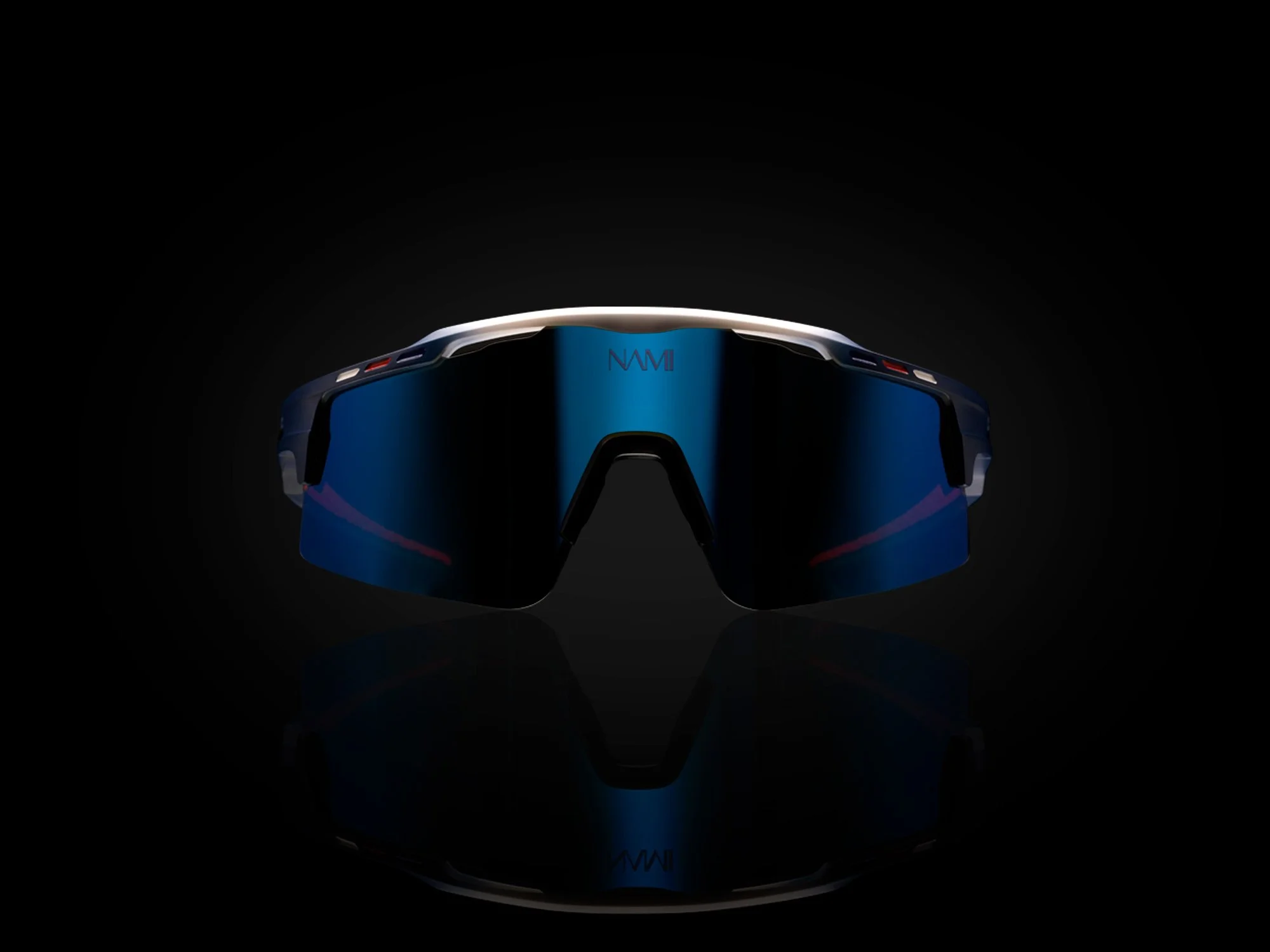 Black sports sunglasses with mirrored blue lenses reflecting a faint red light, set against a black background with a subtle reflection below.
