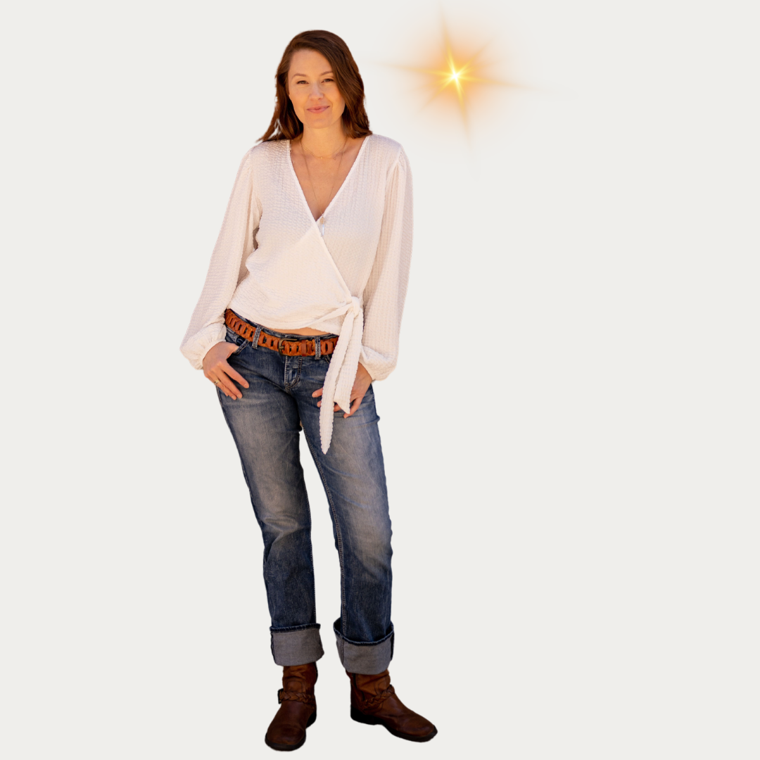 A woman with brown hair wearing a cream-colored blouse, blue jeans, and brown boots, standing against a plain background with a bright star-shaped light near her head.