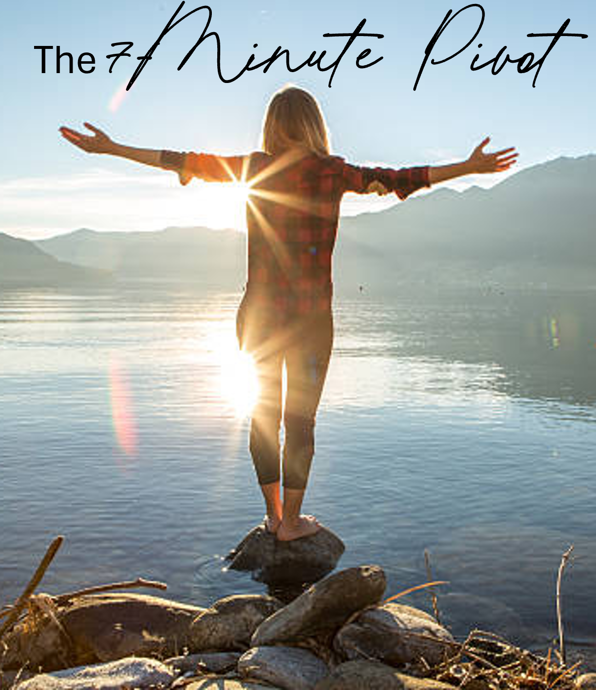 A woman standing on rocks by a lake with arms outstretched, facing the sunrise or sunset over mountains.