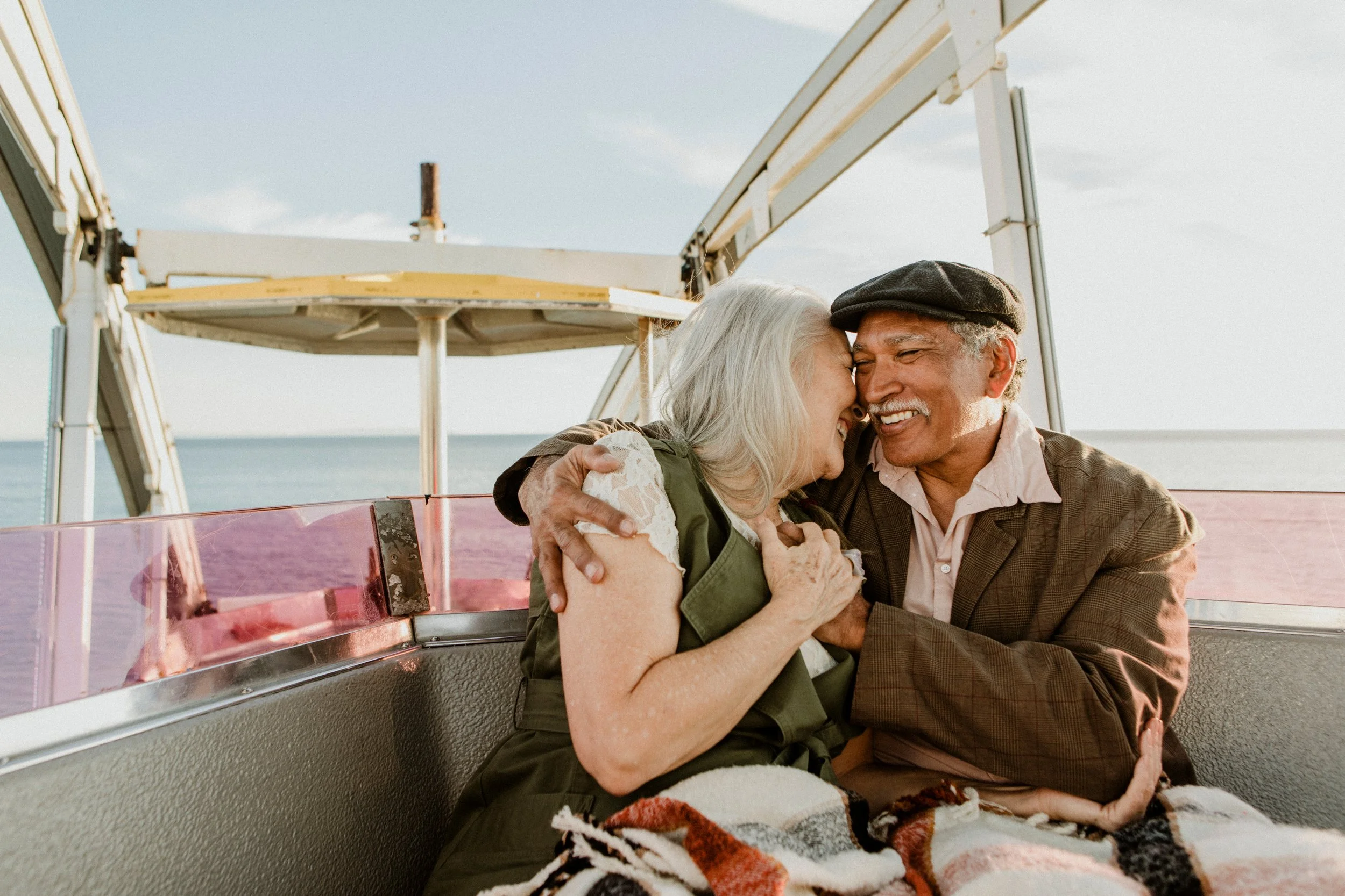 Two older adults sitting together on a Ferris wheel overlooking the water during an outdoor leisure activity in retirement