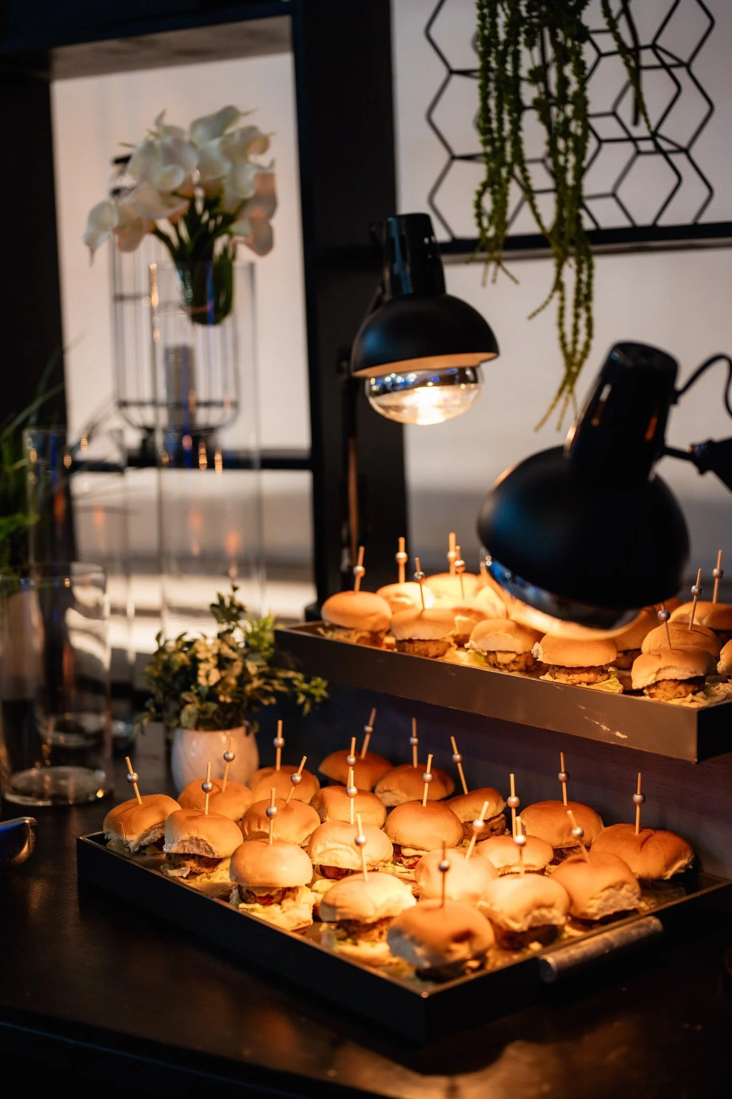 A sophisticated culinary presentation of gourmet mini burgers by ALilBitOfThatSpice, showcased under warm lighting, ready to delight guests at a My Dream Party Productions event. The attention to detail reflects a fusion of high-quality catering and