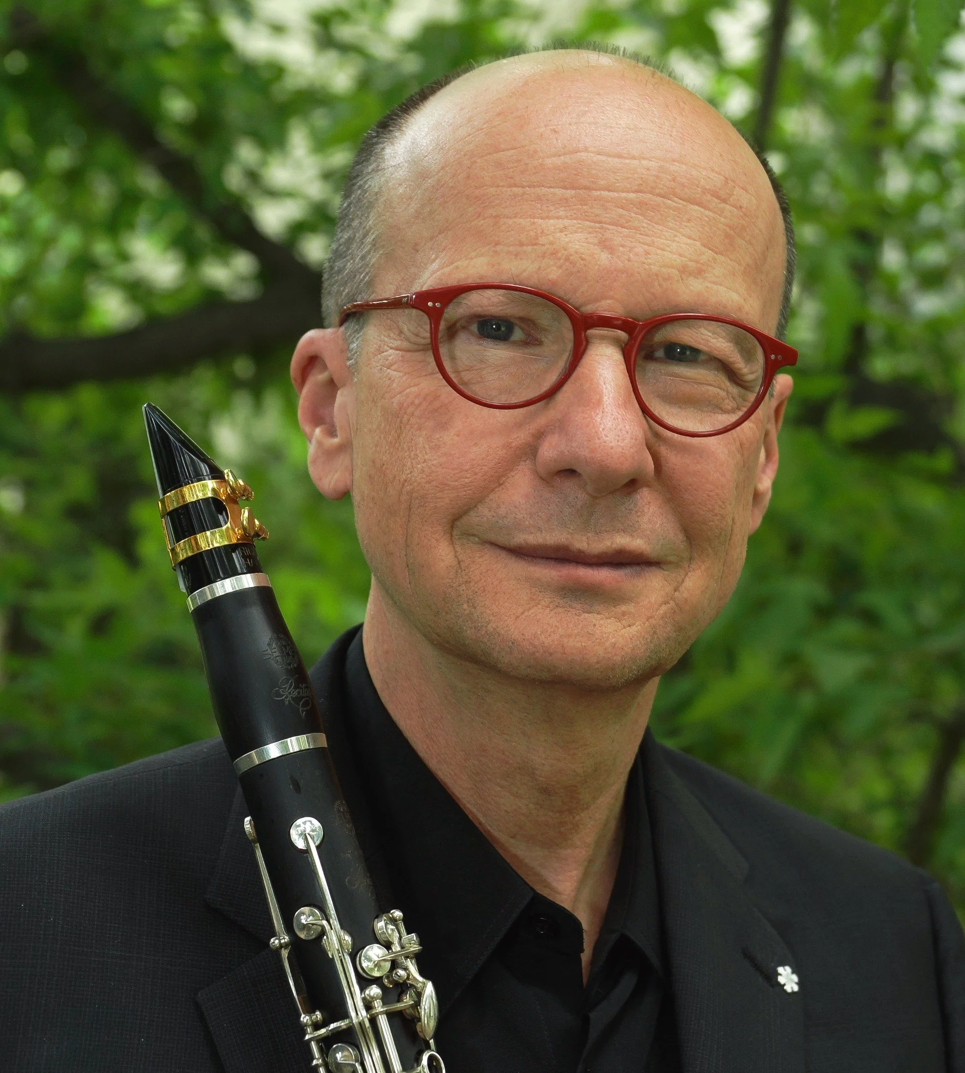 Clarinetist James Campbell headshot in front of trees with clarinet