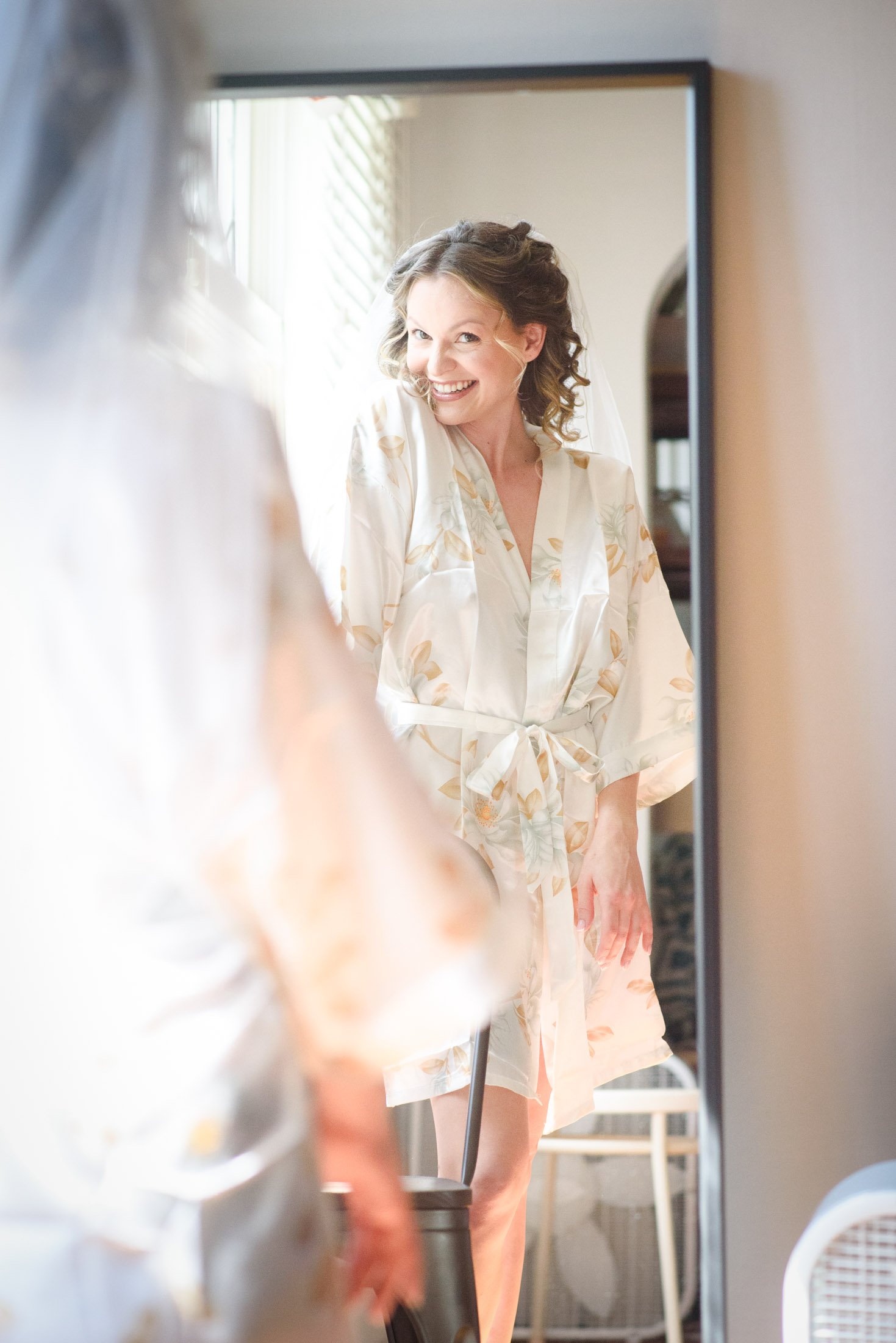 Wedding photo at Hoyt Arboretum of A woman in a floral silk robe smiling as she looks at herself in a mirror.