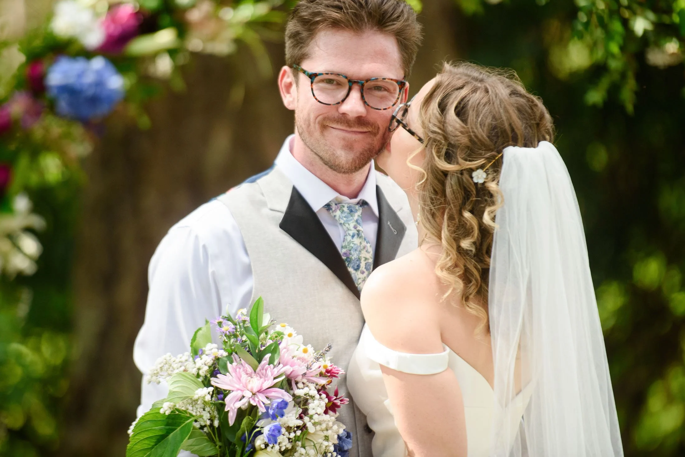 Wedding photo at Hoyt Arboretum of A bride and groom sharing a tender moment outdoors on their wedding day, with the bride whispering into the groom's ear. 