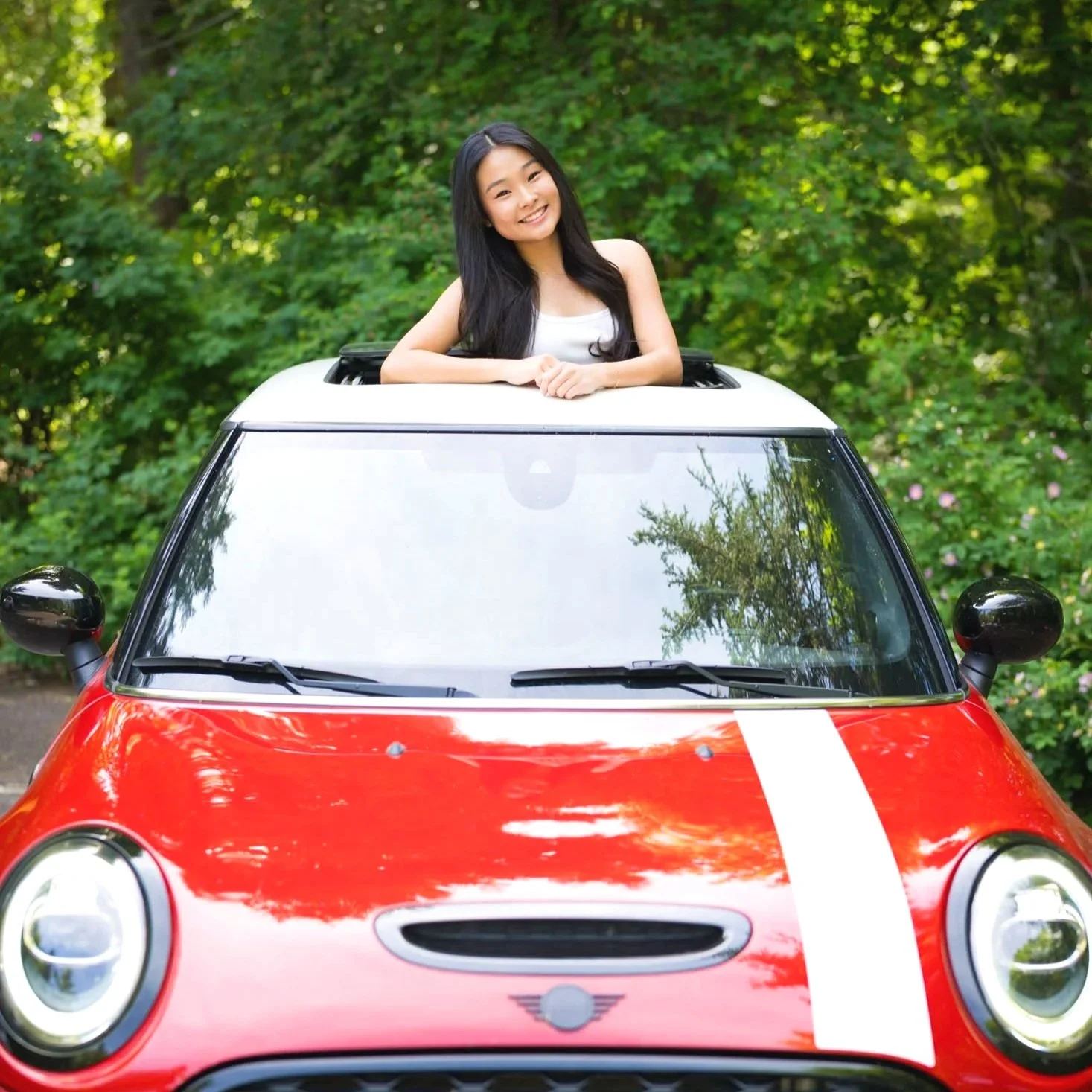 A young woman standing in the sun roof of her Mini Cooper for her senior photos in Portland, Oregon.