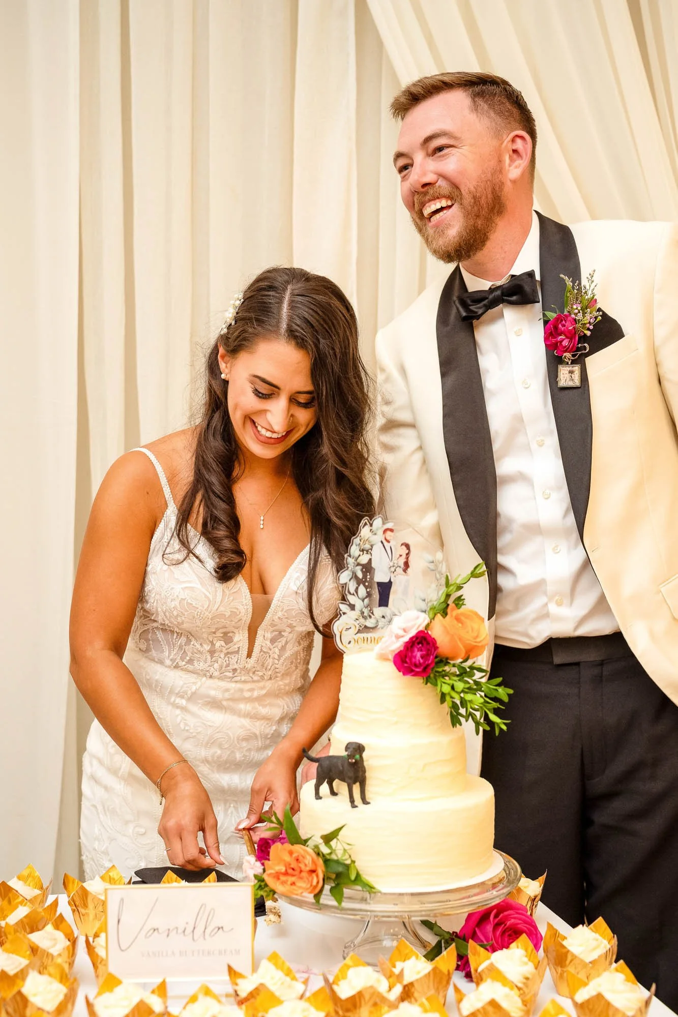 Wedding photo at Abernethy Center's Abernethy Chapel of Bride and groom celebrating, smiling near a wedding cake on a table with cupcake wrappers, flowers, and a cake topper with couple figurines. 