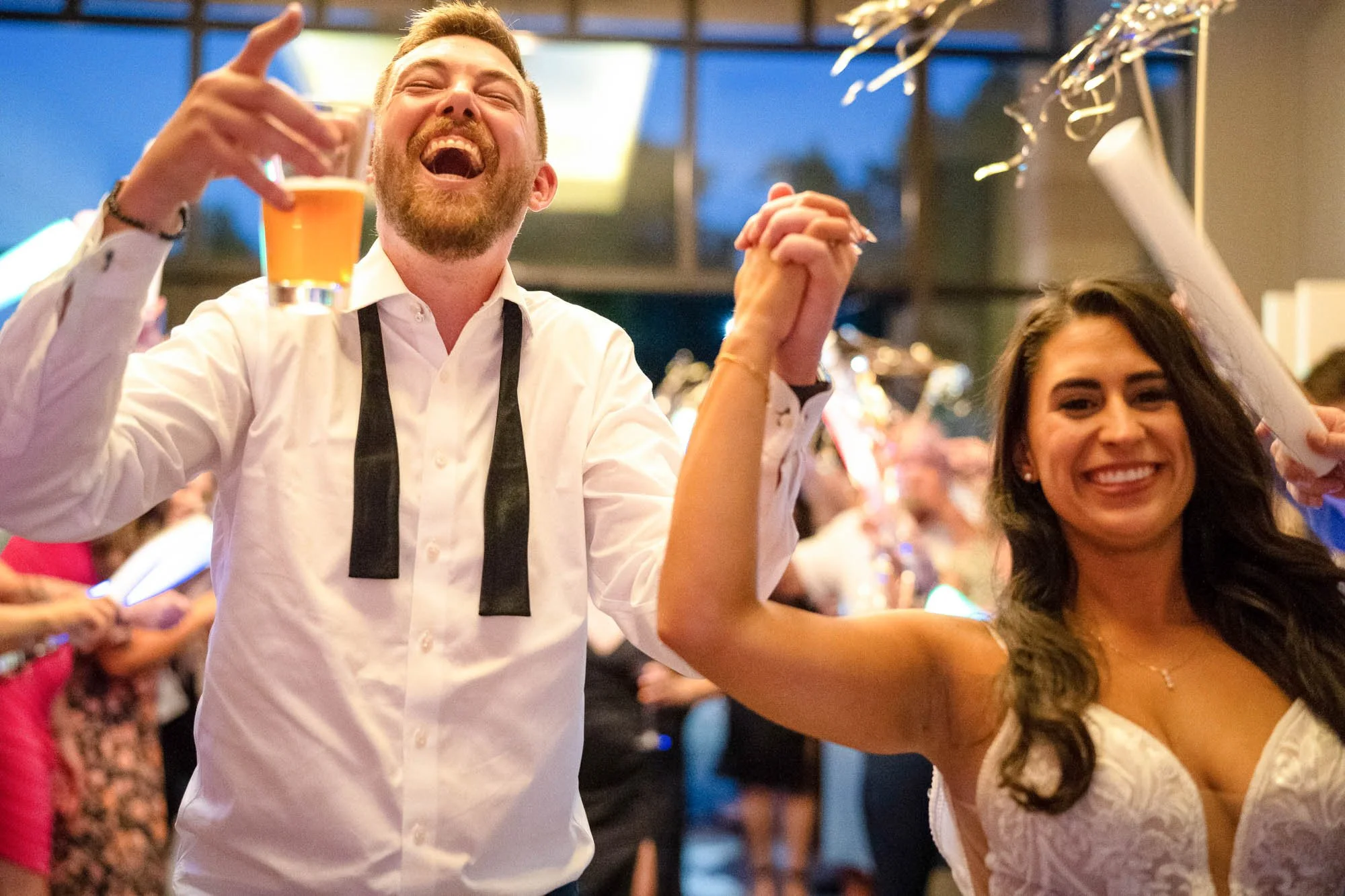 Wedding photograph at Abernethy Center Veiled Garden and Ballroom of Happy man and woman celebrating at a party, holding hands up with drinks, smiling and enjoying the moment.