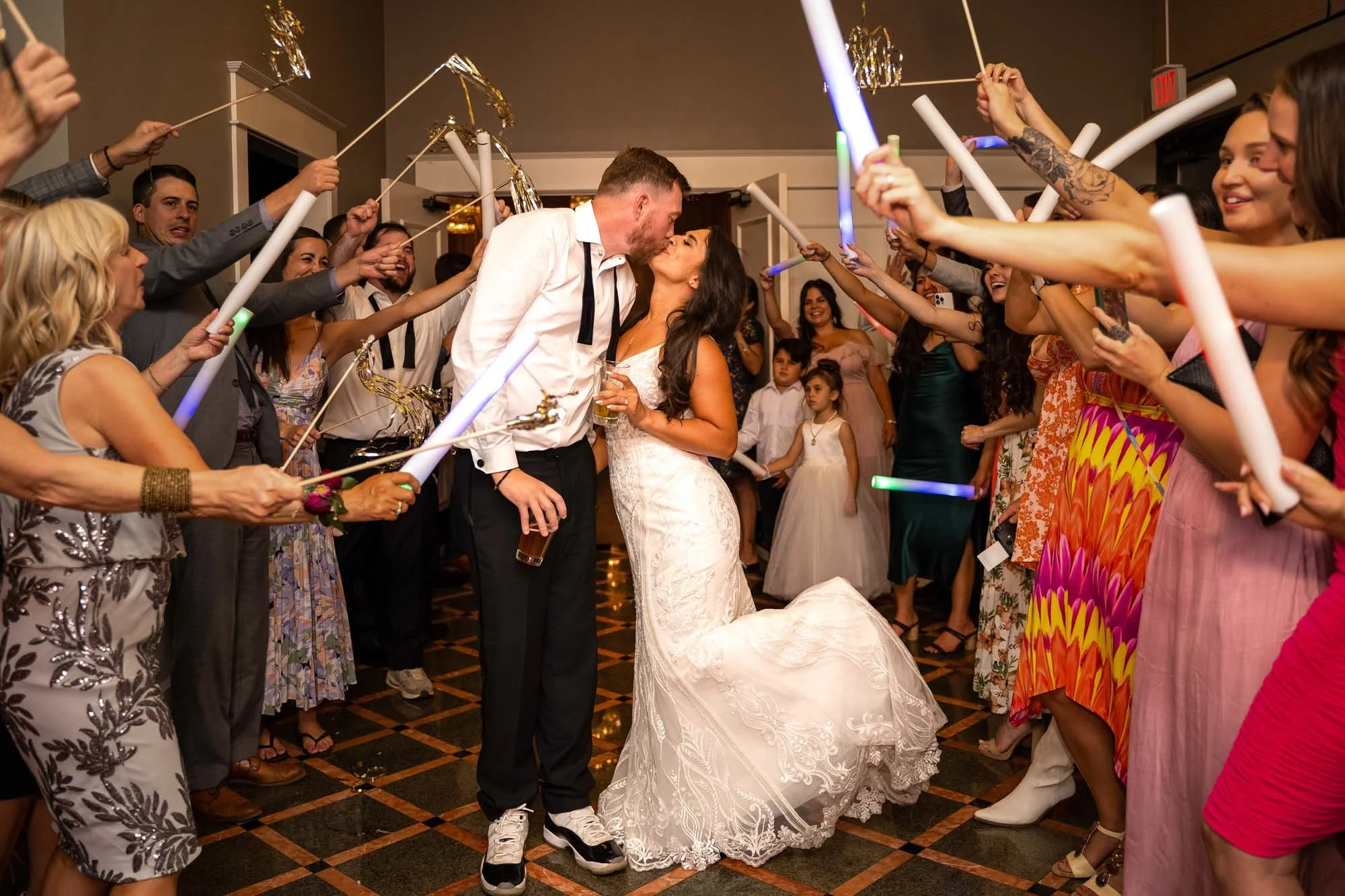 Wedding photos at Abernethy Center Veiled Garden and Ballroom of A bride and groom kiss during their wedding reception while guests surround them, holding glowing light sticks and celebrating.
